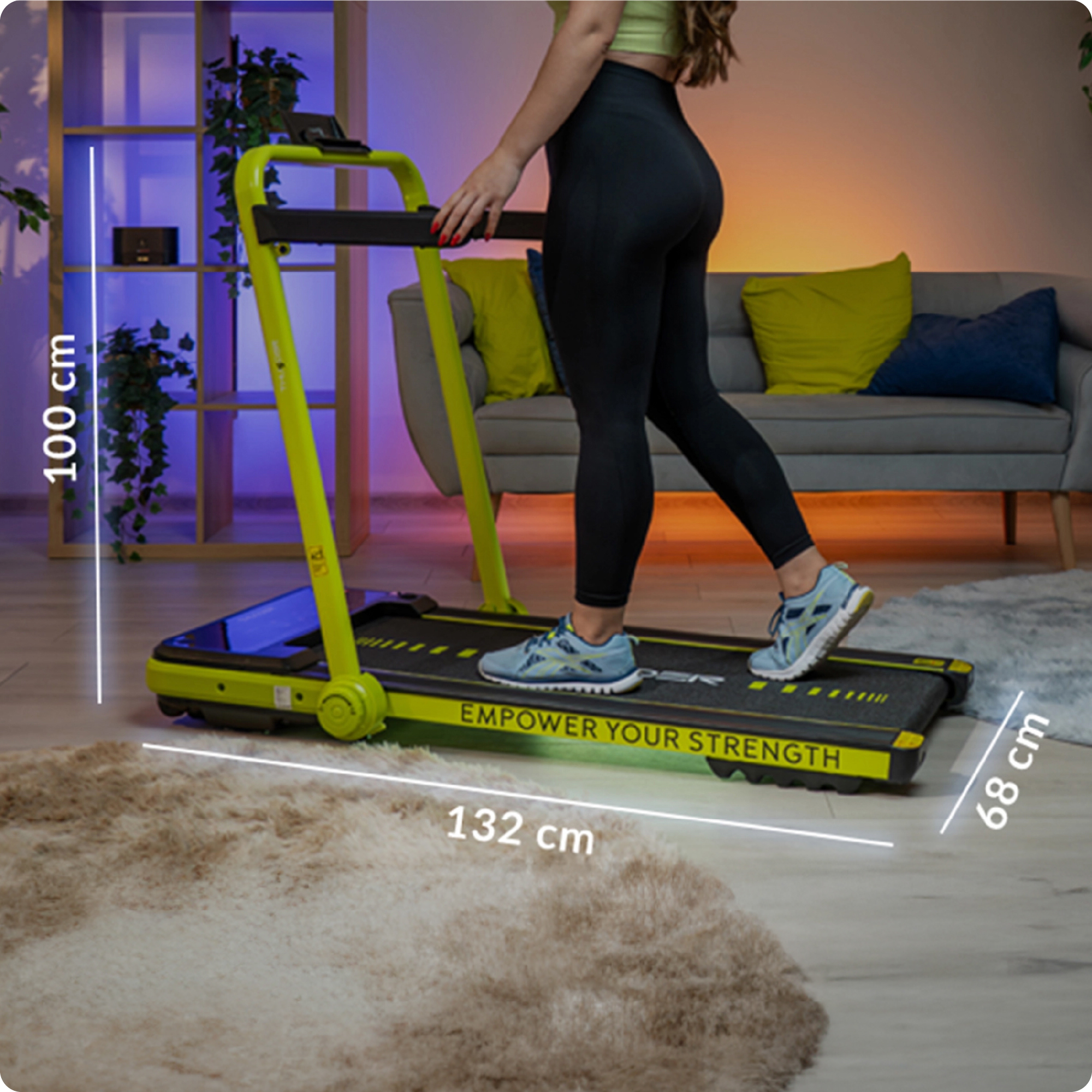 Kobieta stoi na zielonej bieżni, której wymiary to 100 cm wysokości i 132 cm długości.