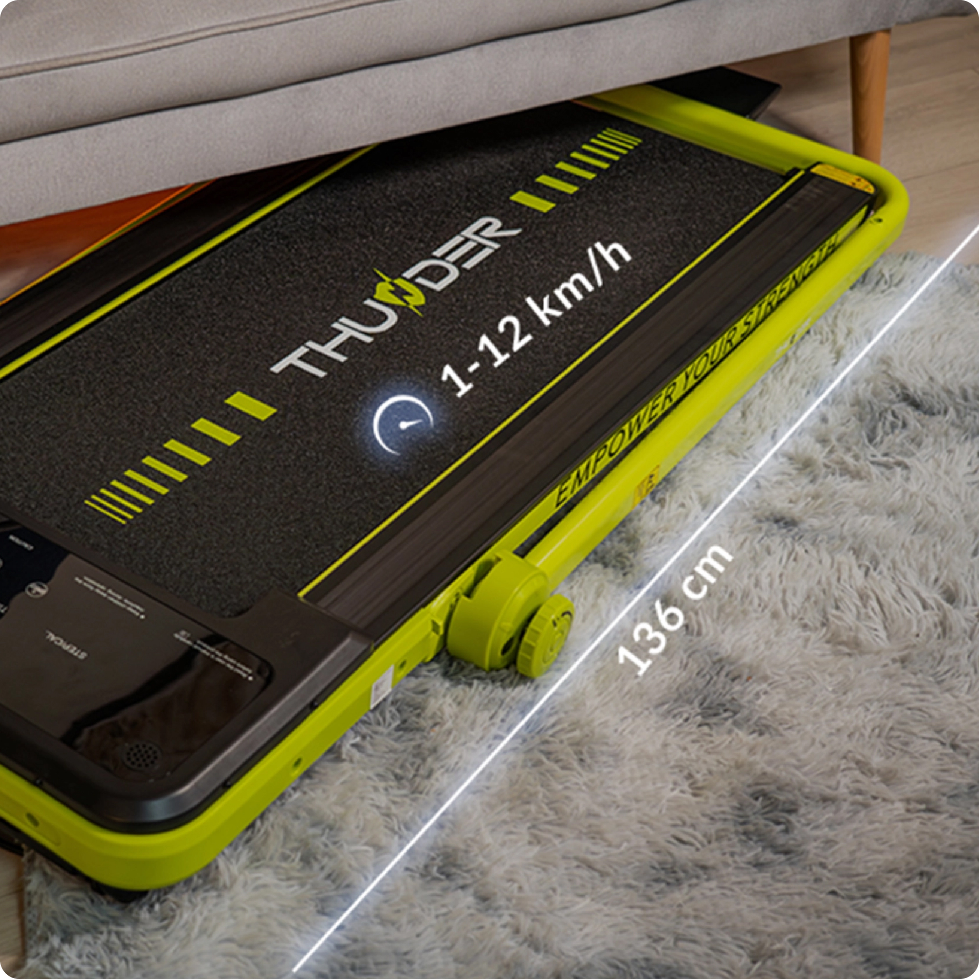 Zielona bieżnia jest umieszczona pod kanapą, z wymiarami oznaczonymi jako 136 cm długości i zakresem prędkości 1-12 km/h.