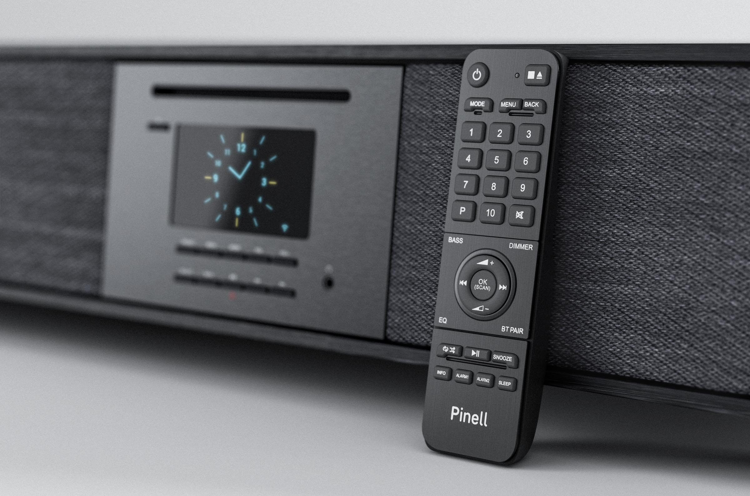 A remote control rests next to a black audio device. The device has a display showing a clock.