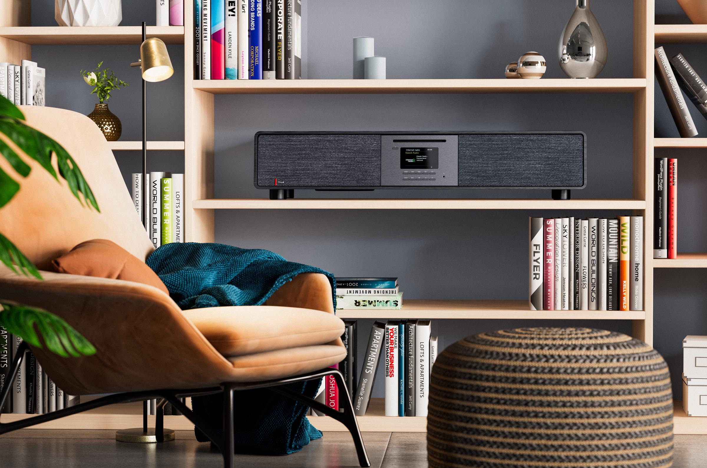A black audio device sits on a shelf amidst books and a chair in a well-lit room.