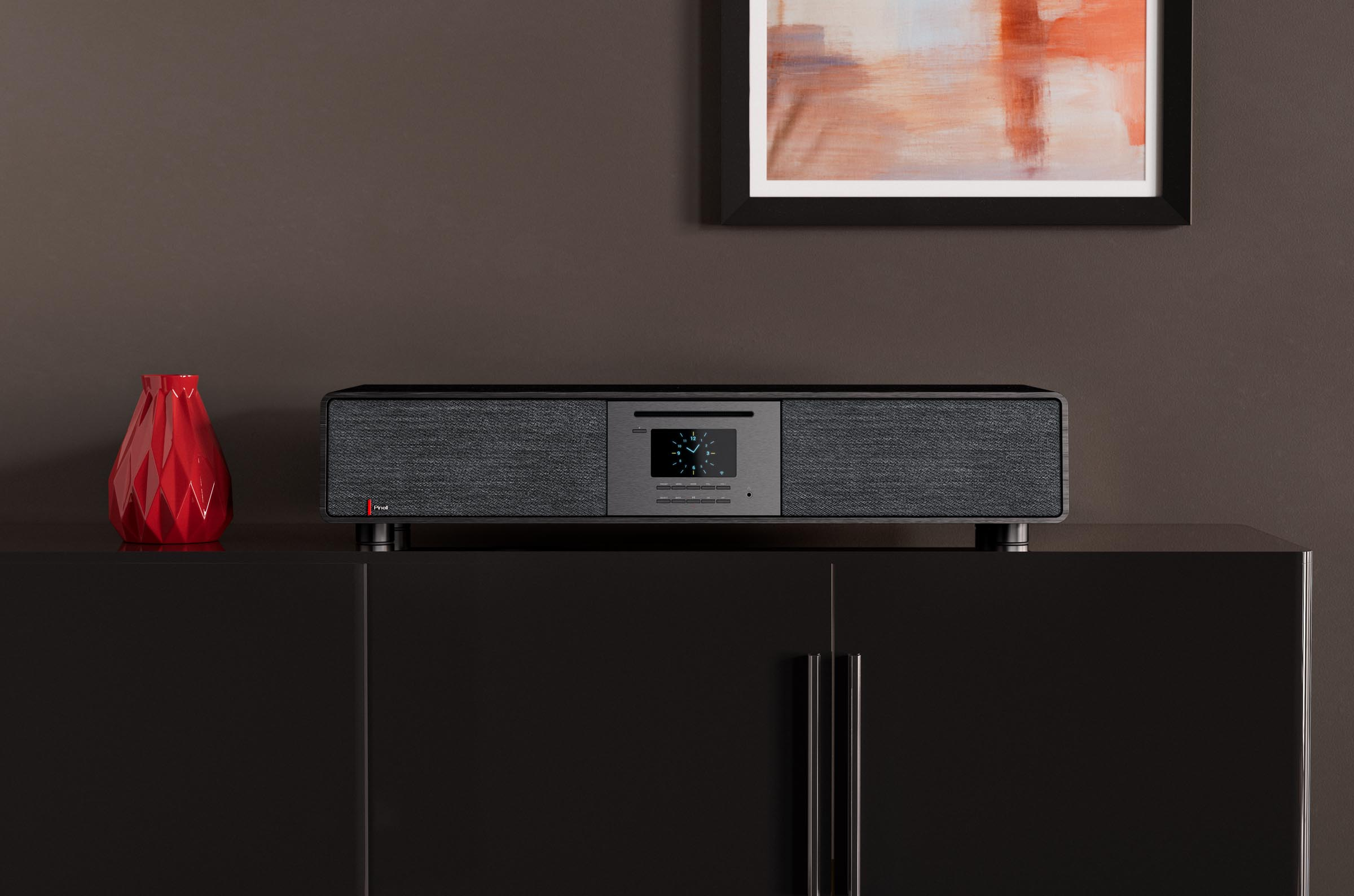 A black audio device sits on a black cabinet against a brown wall with framed art and a red vase.