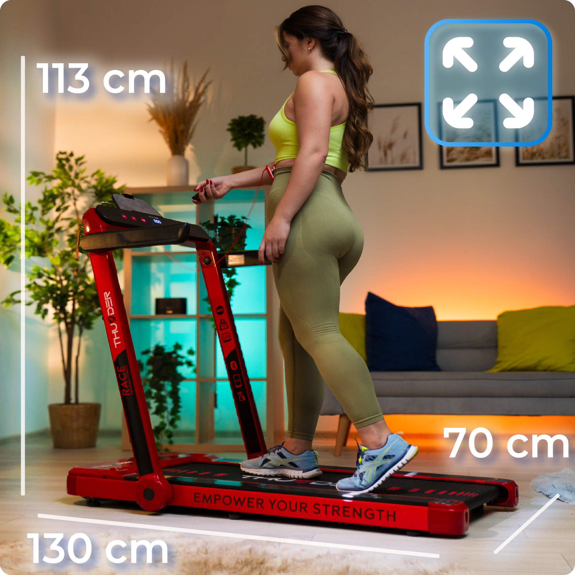 Kobieta w stroju sportowym używa czerwonej bieżni, z wymiarami i ikoną powiększenia.