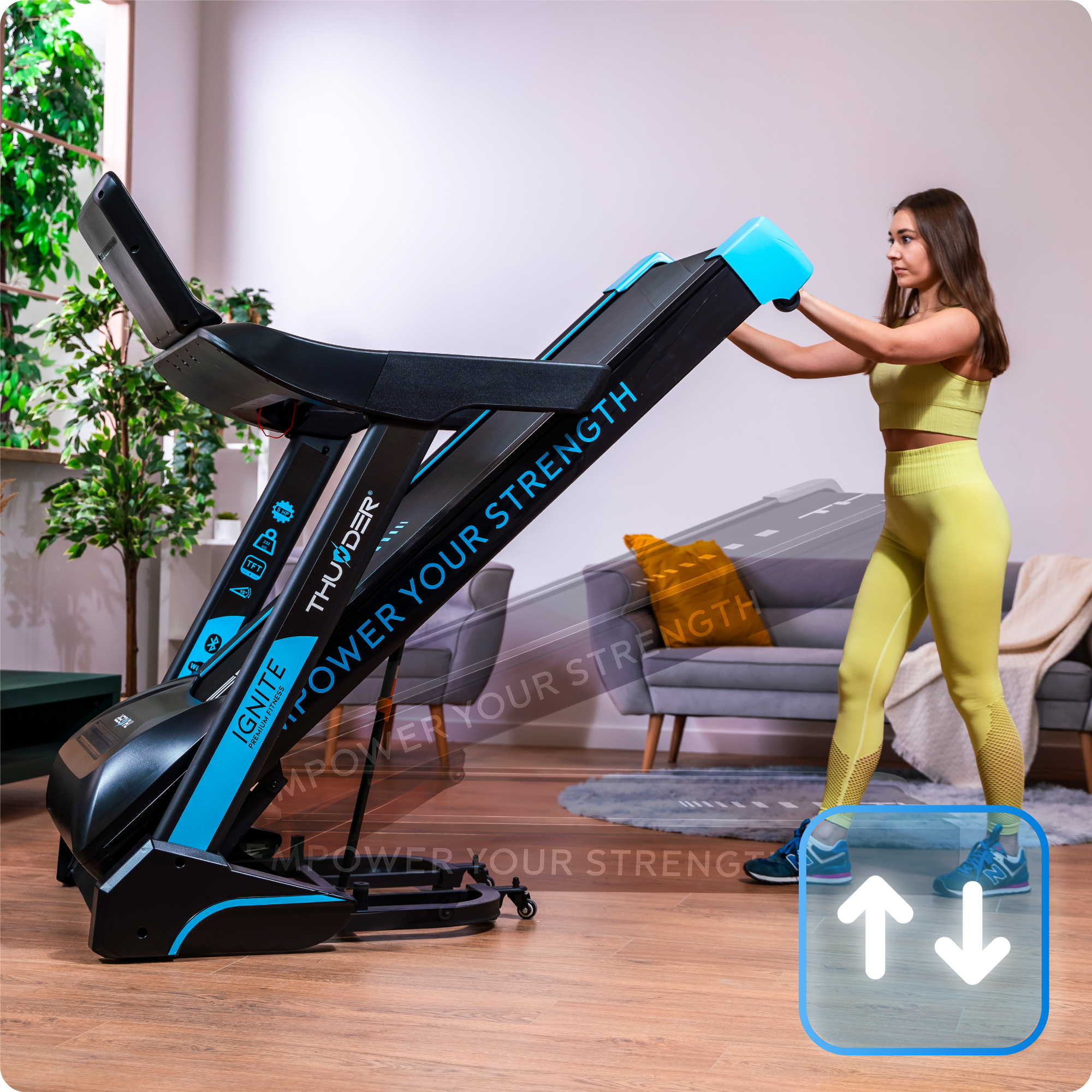 Kobieta składa czarno-niebieską bieżnię w salonie z szarą kanapą.