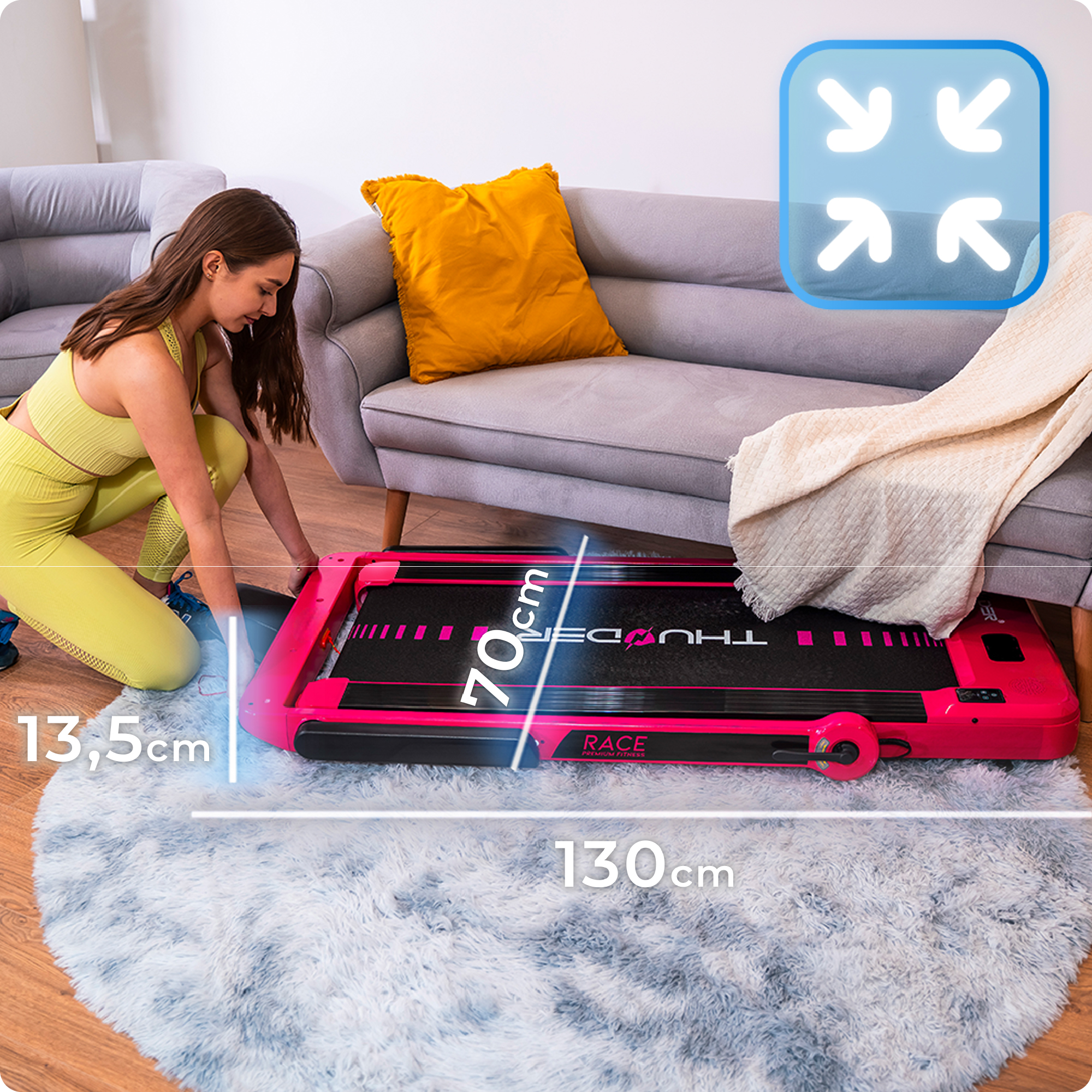 Kobieta składa różową bieżnię w salonie z szarą kanapą i puszystym dywanem.