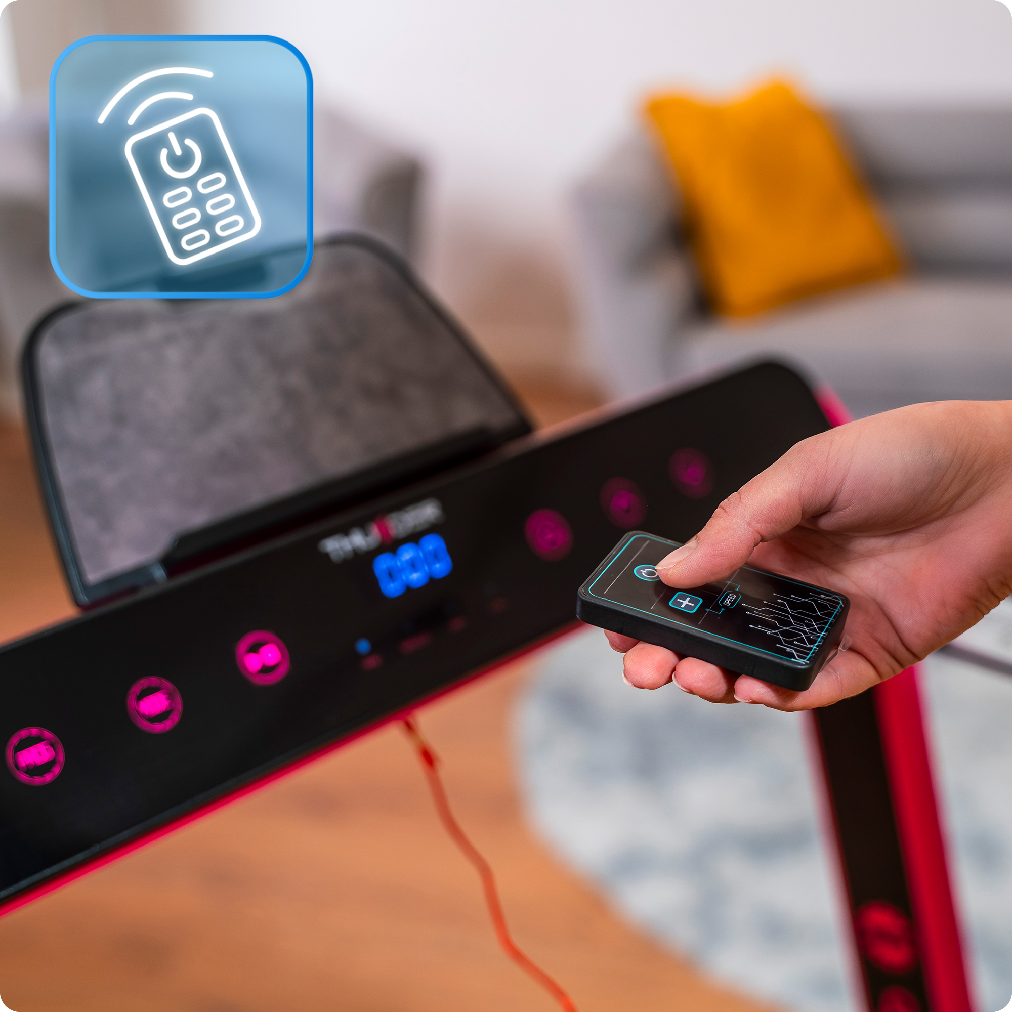 Ręka trzyma pilota w pobliżu różowej bieżni z szarą konsolą i niebieskim wyświetlaczem w jasnym, nowoczesnym salonie.