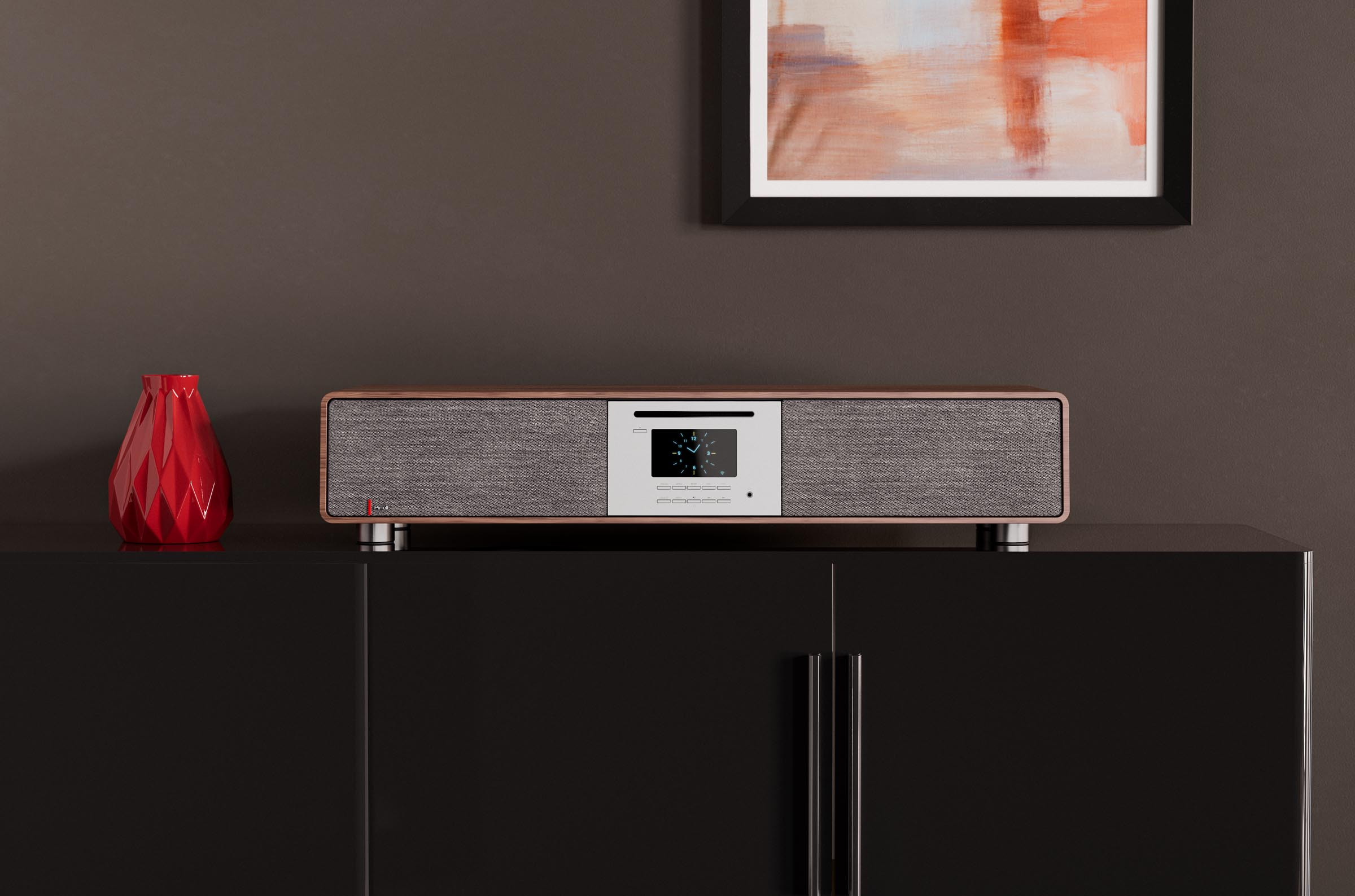 Stereo system on a black cabinet, red vase, and a painting on a brown wall.
