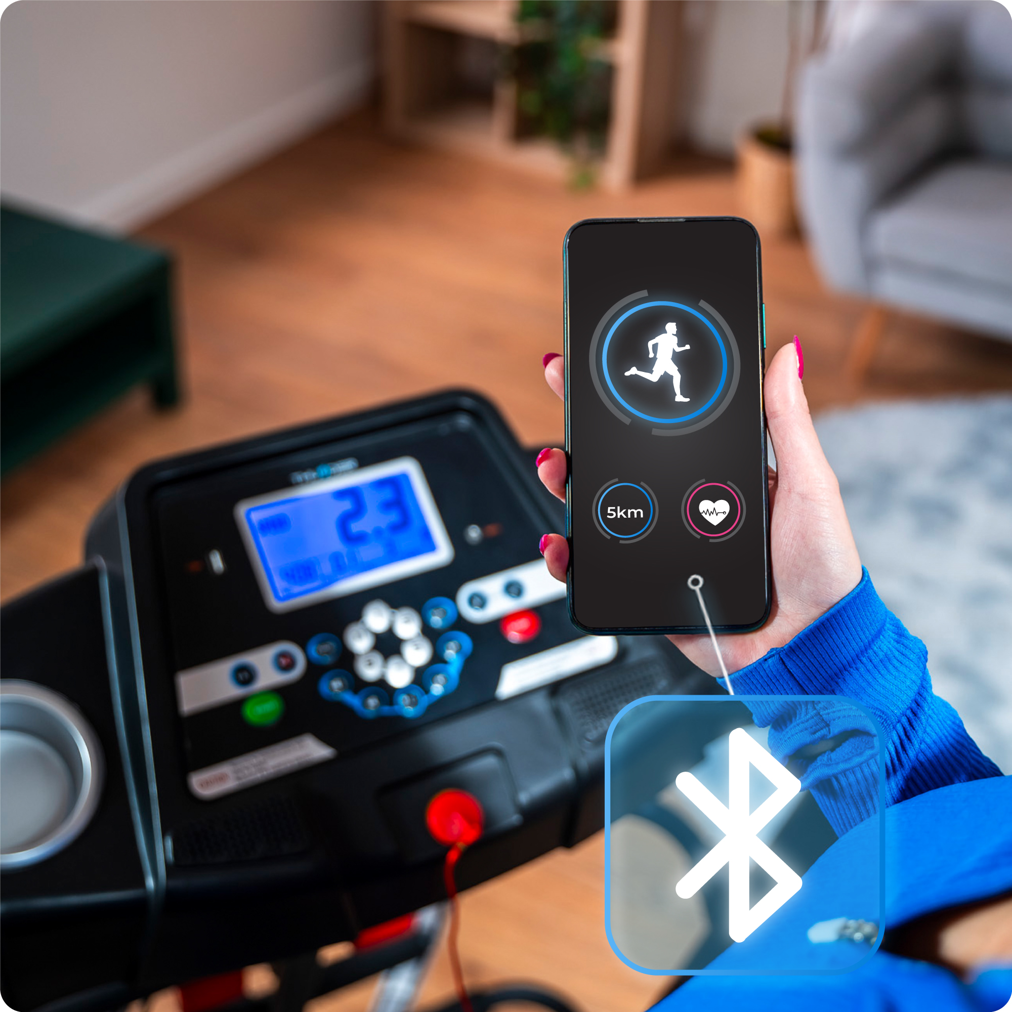 Bieżnia z cyfrowym wyświetlaczem i ręką trzymającą telefon z aplikacją do biegania z symbolem Bluetooth.