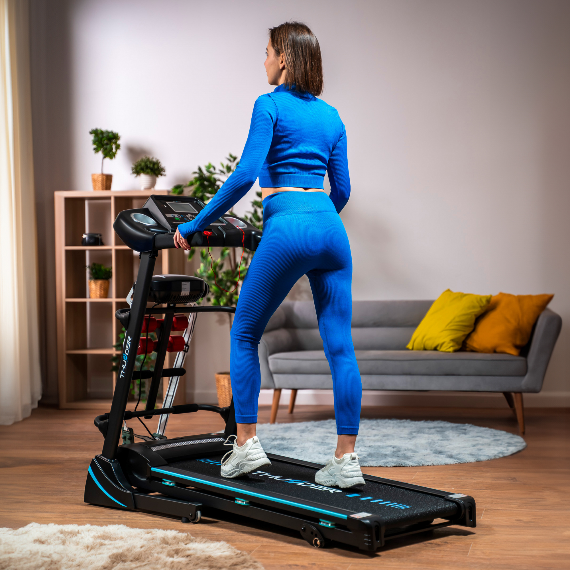 Kobieta w niebieskim stroju do ćwiczeń na czarnej bieżni z niebieskimi akcentami w salonie.