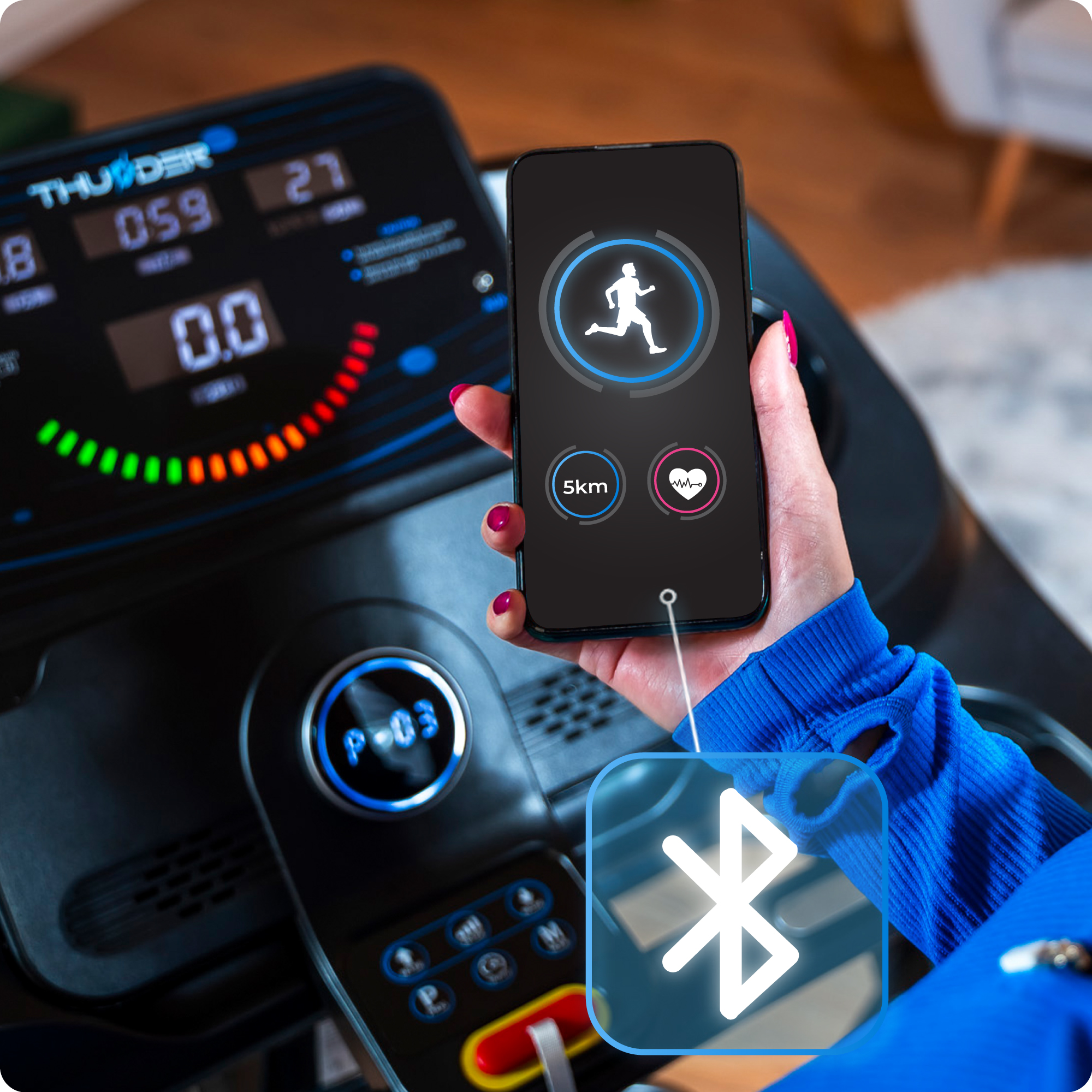 Zbliżenie kobiety trzymającej telefon z aplikacją fitness, z widoczną konsolą bieżni i ikoną Bluetooth.