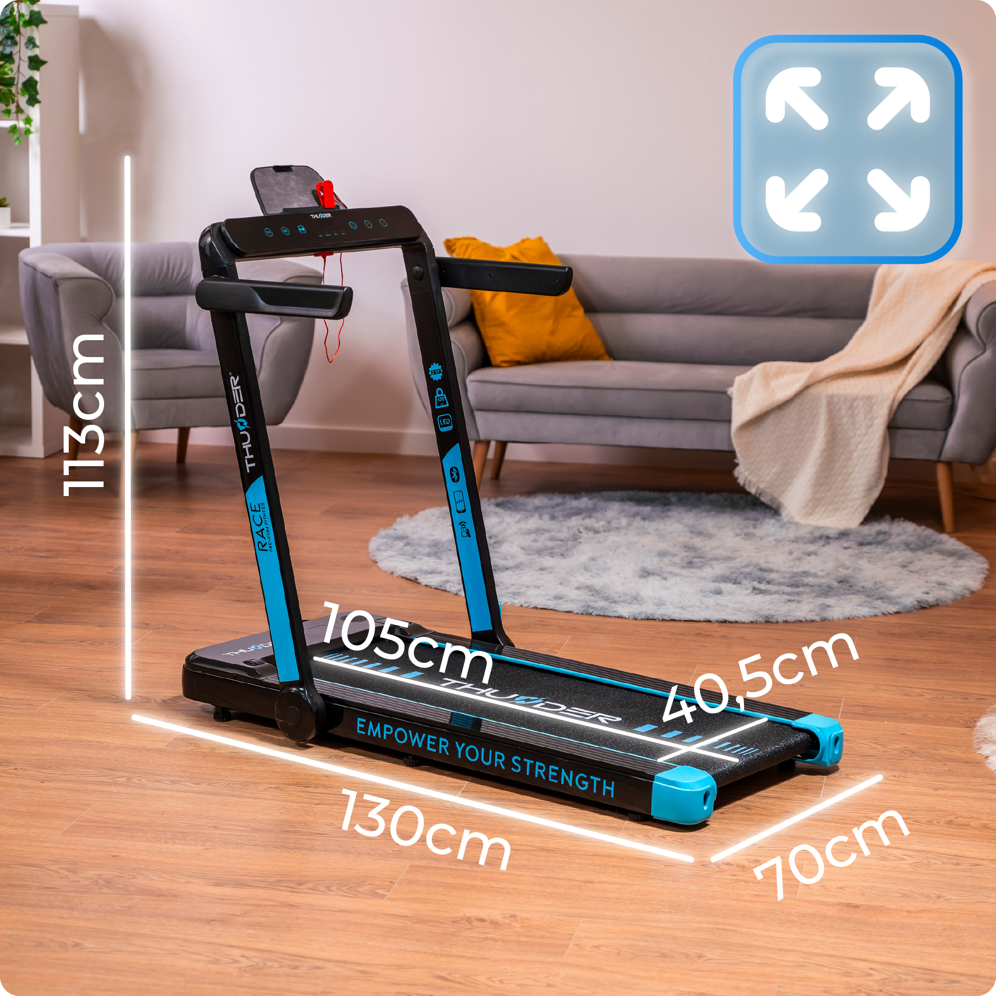 Czarno-niebieska bieżnia z oznaczonymi wymiarami w salonie z sofą i dywanem w tle.