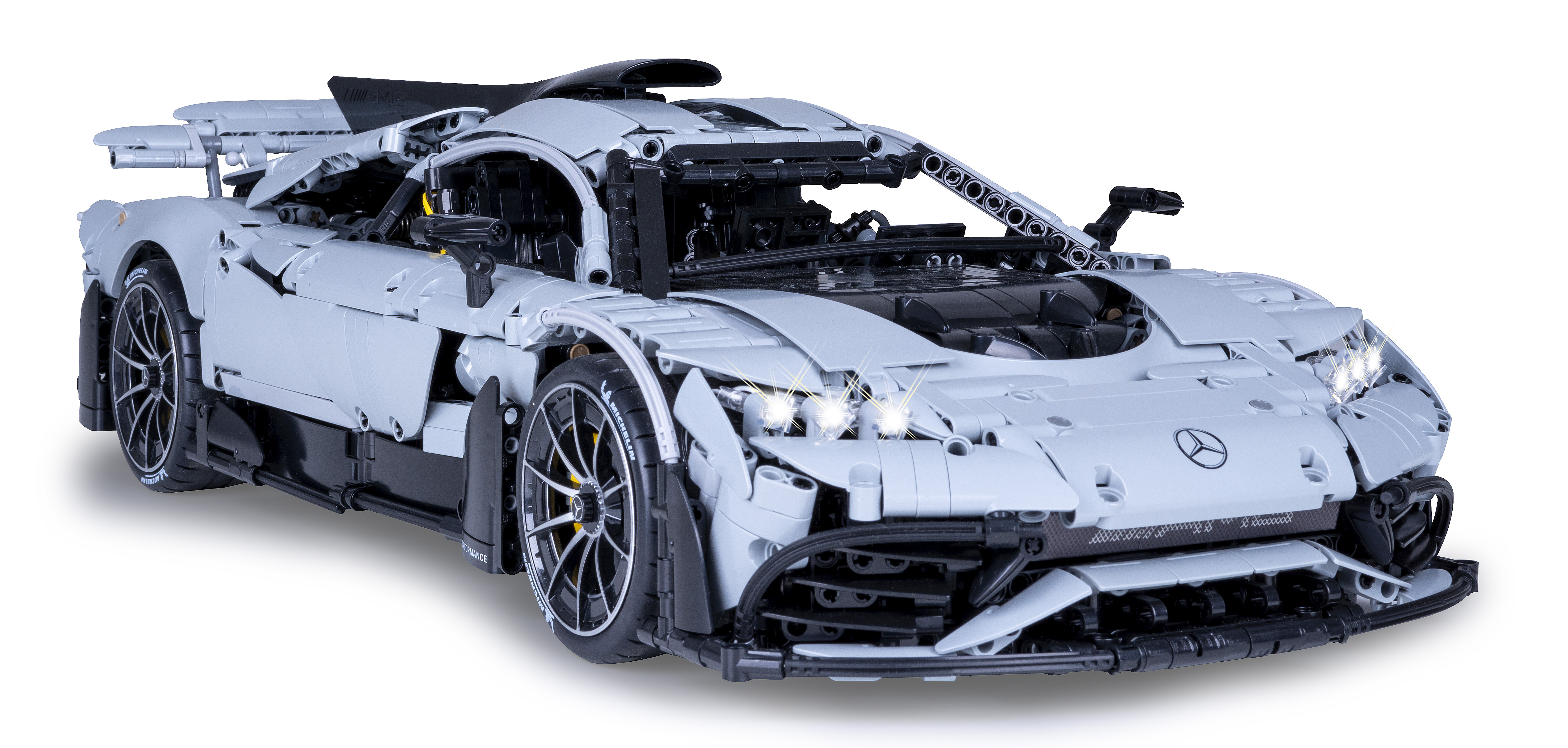 Ein hellgraues Spielzeugauto mit filigranen Details, eingeschalteten Scheinwerfern, vor einem sauberen weißen Hintergrund.