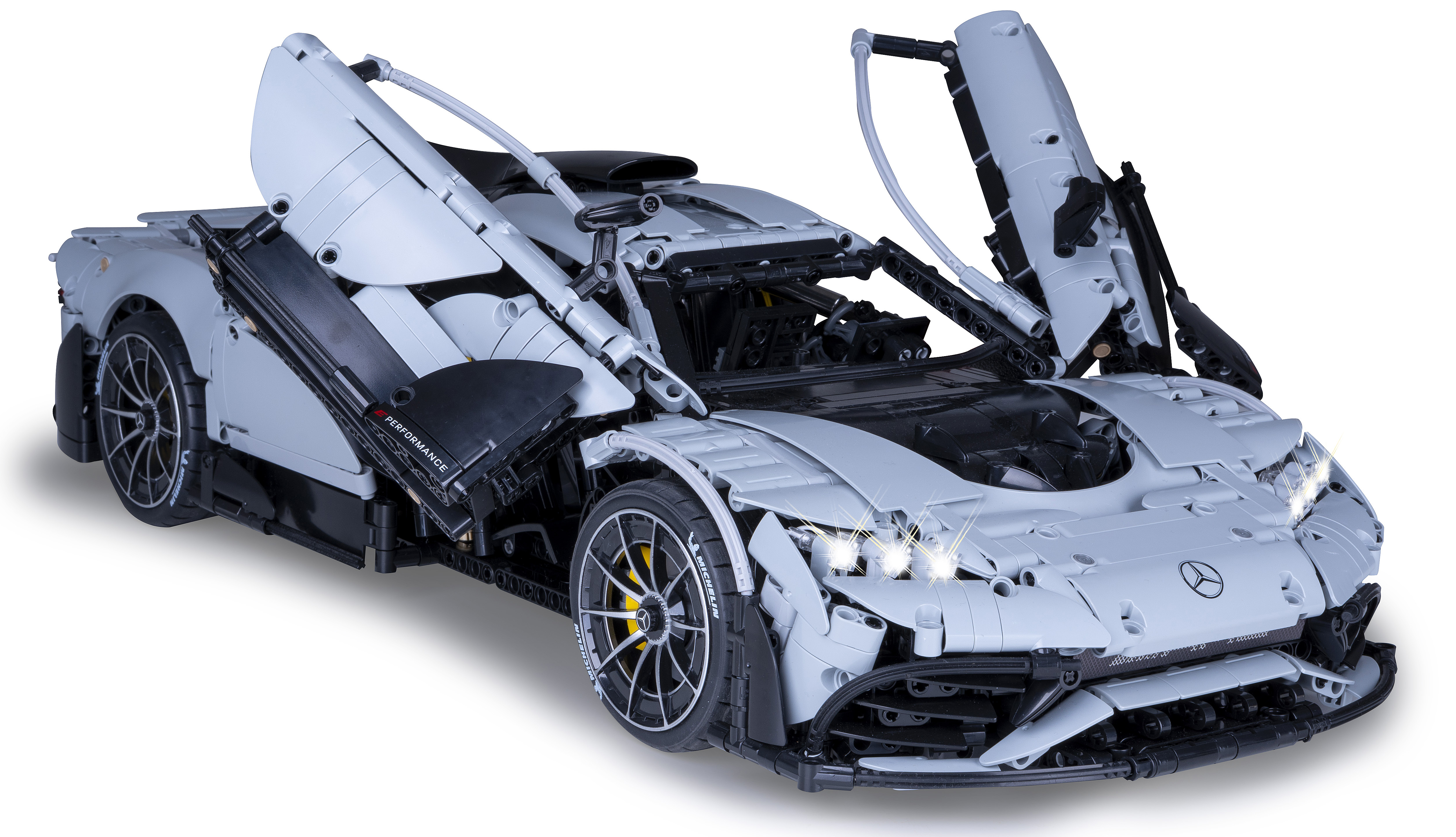 Ein grauer Lego Mercedes-AMG ONE mit offenen Türen und leuchtenden Scheinwerfern auf weißem Hintergrund.