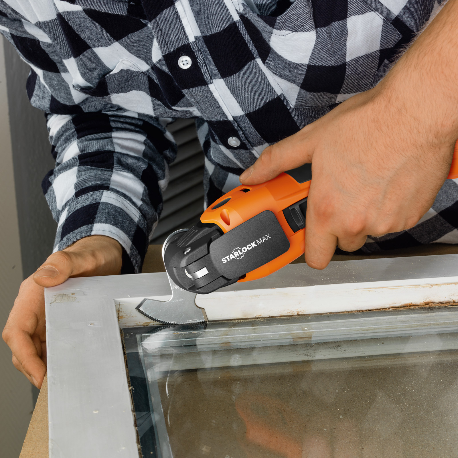 Eine Person benutzt ein orangefarbenes Elektrowerkzeug, um einen weißen Rahmen mit Glas zu schneiden.