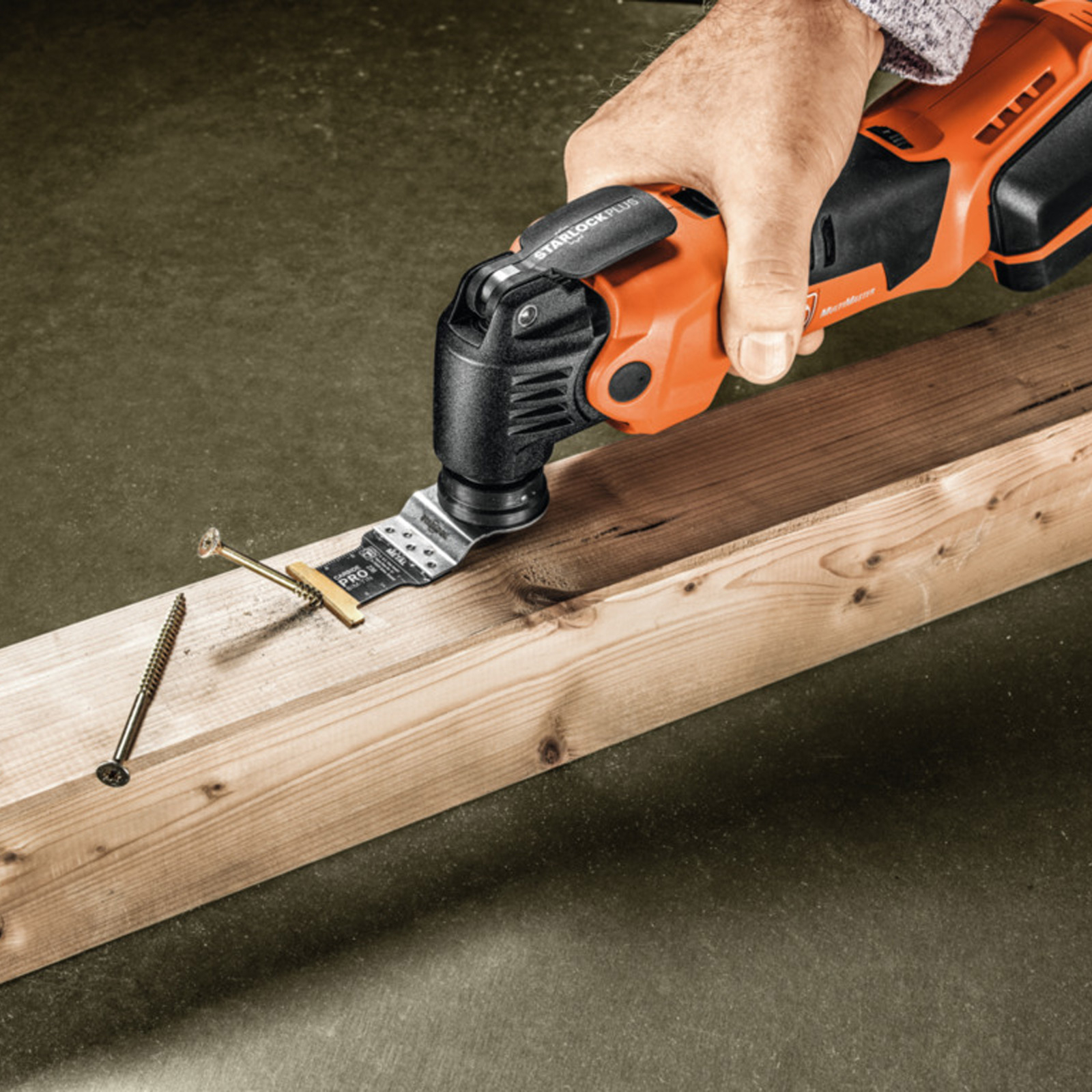 Eine Person benutzt ein orangefarbenes Multitool, um eine Holzplanke mit Nägeln zu schneiden.