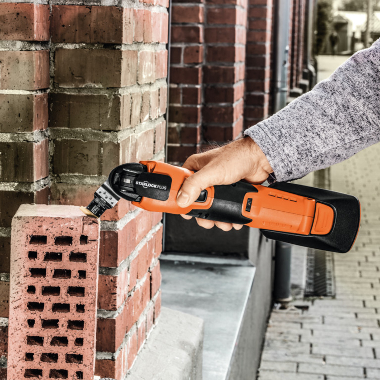 Eine Person schneidet einen Ziegelstein mit einem orangefarbenen oszillierenden Multitool.
