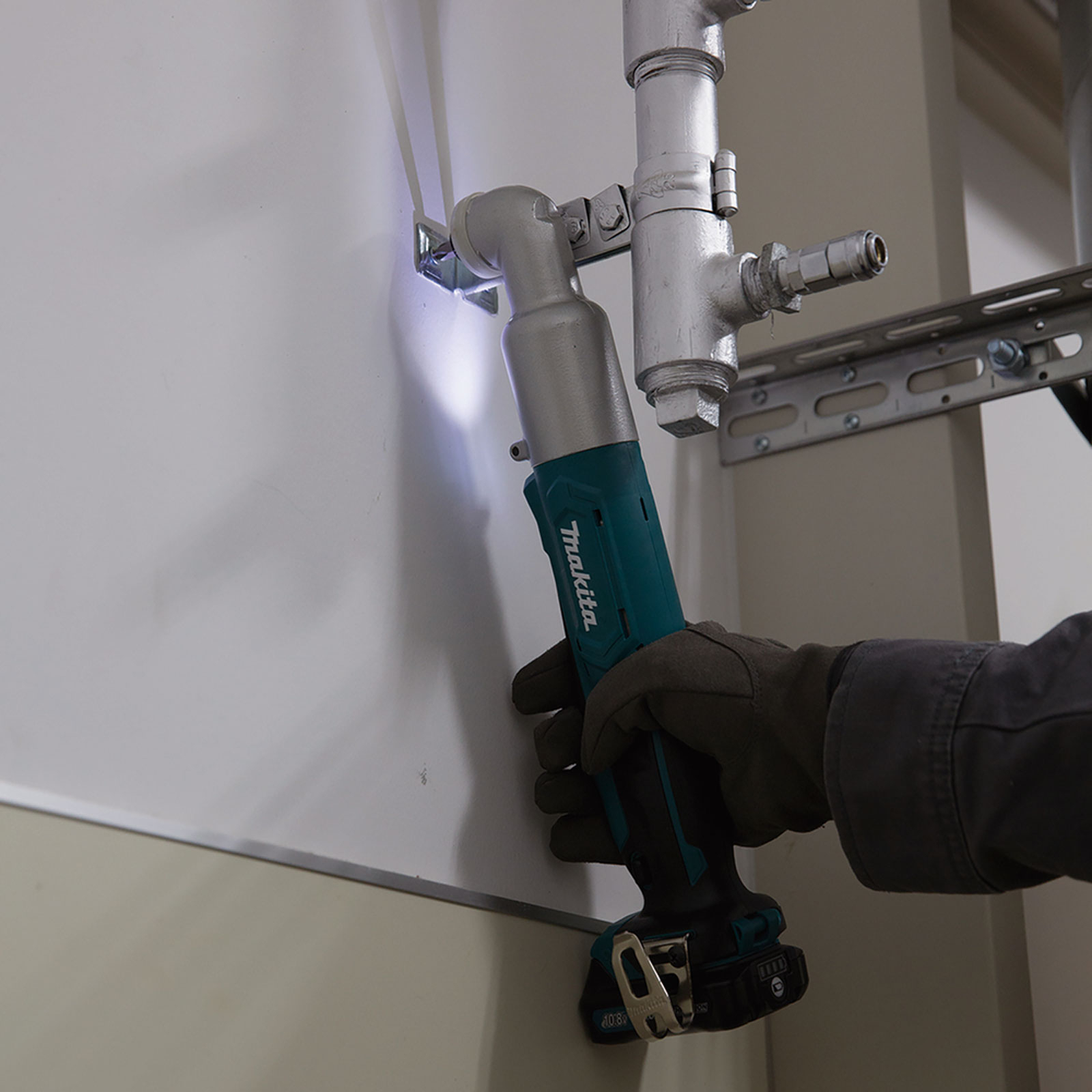 Se está utilizando un taladro Makita turquesa y negro para perforar una tubería cerca de una pared blanca.