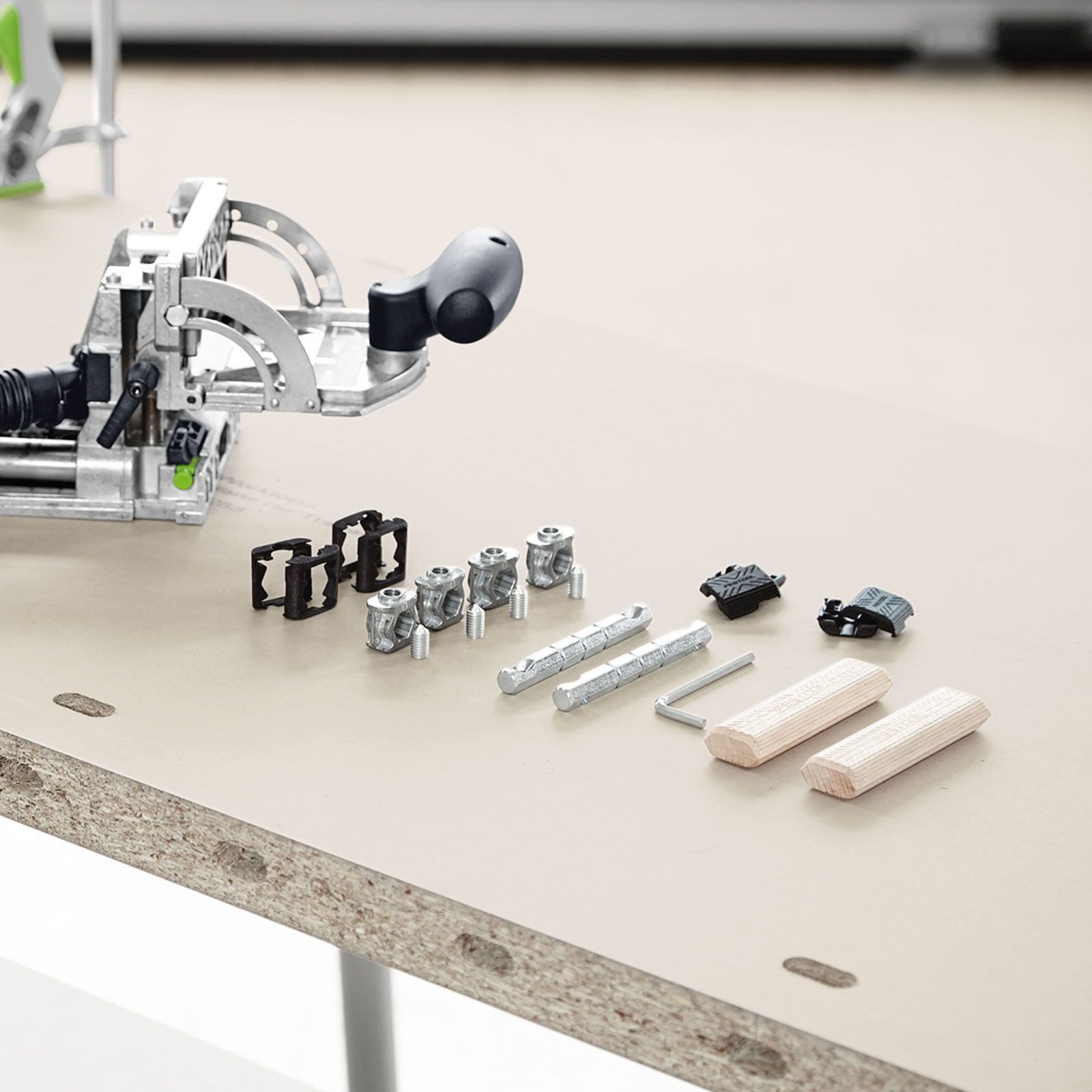 Srebrna strugarka Domino z kołkami i elementami montażowymi na płowej powierzchni.