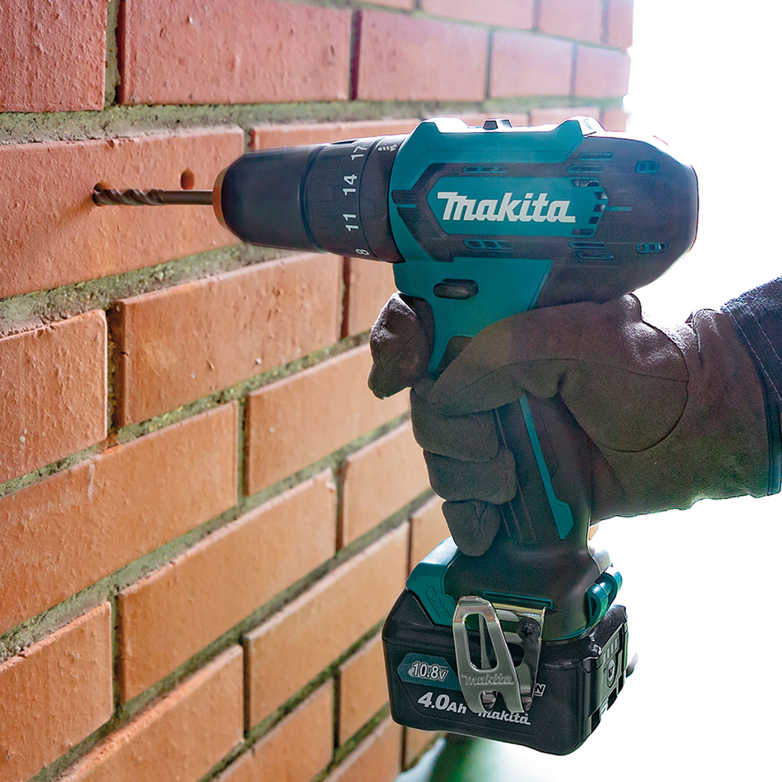 Un taladro Makita negro y verde azulado está perforando una pared de ladrillo rojo.