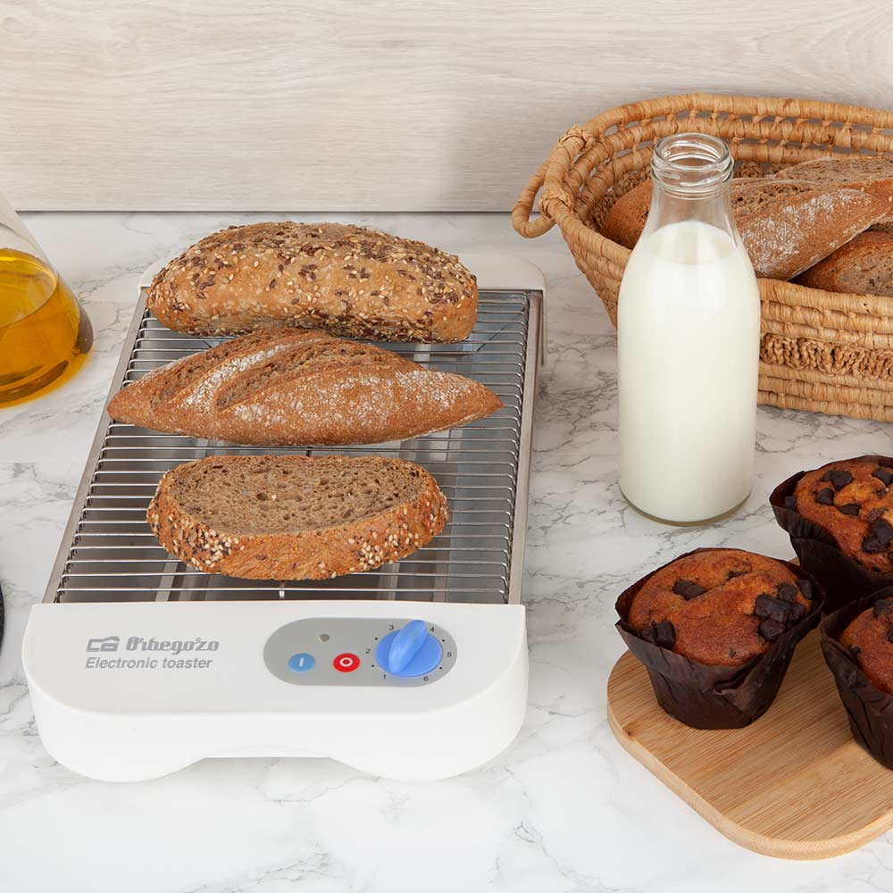 Tostadora con pan, muffins y una botella de leche sobre una superficie de mármol.