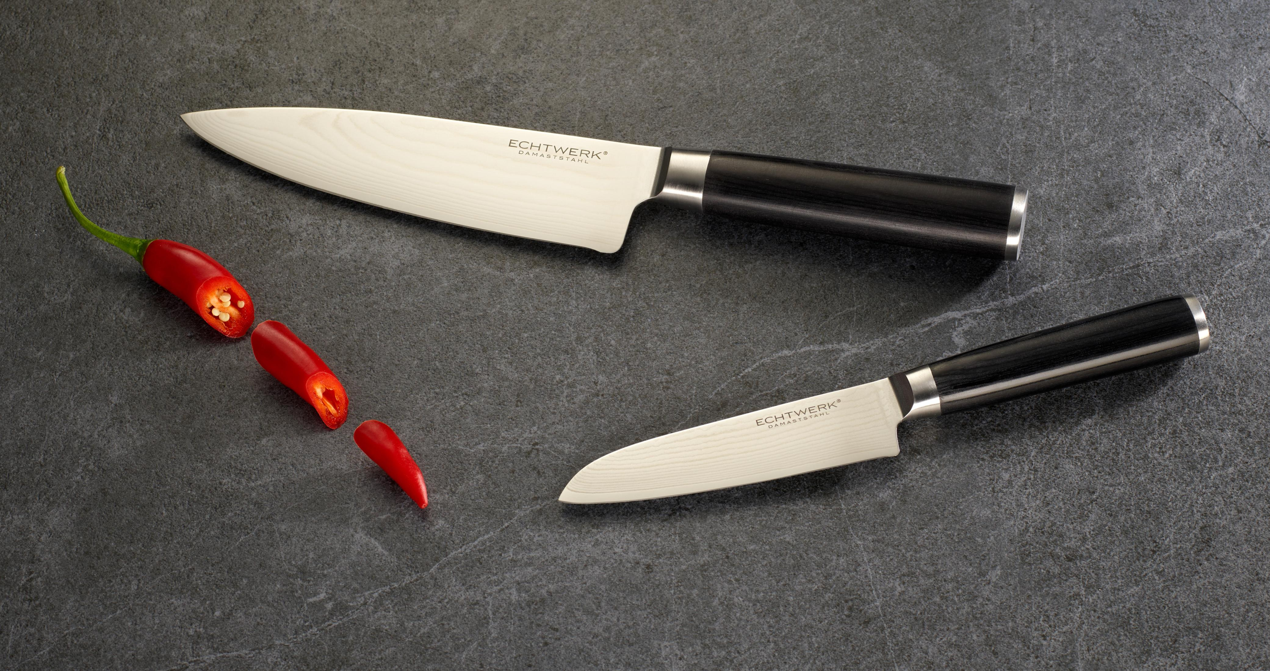 Zwei Messer und geschnittene rote Paprika sind auf einer grauen Oberfläche angeordnet, die kulinarische Werkzeuge hervorhebt.