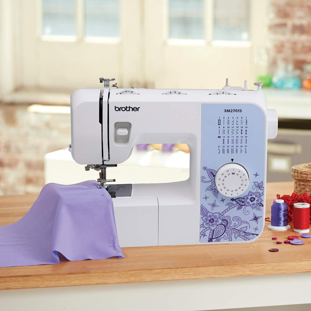 Eine weiße Nähmaschine Brother XM2701S steht mit lila Stoff auf einem Holztisch.