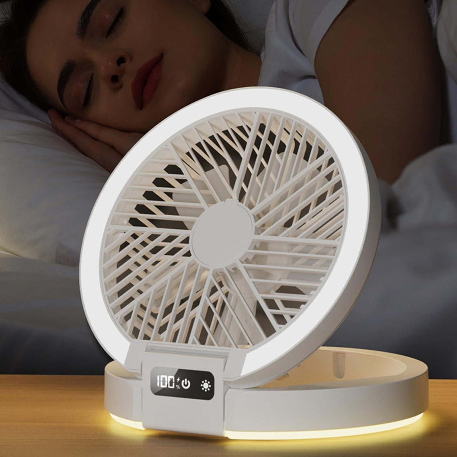 Eine schlafende Frau neben einem weißen, runden Ventilator mit LED-Beleuchtung. Der Ventilator zeigt 100 % Akku an.