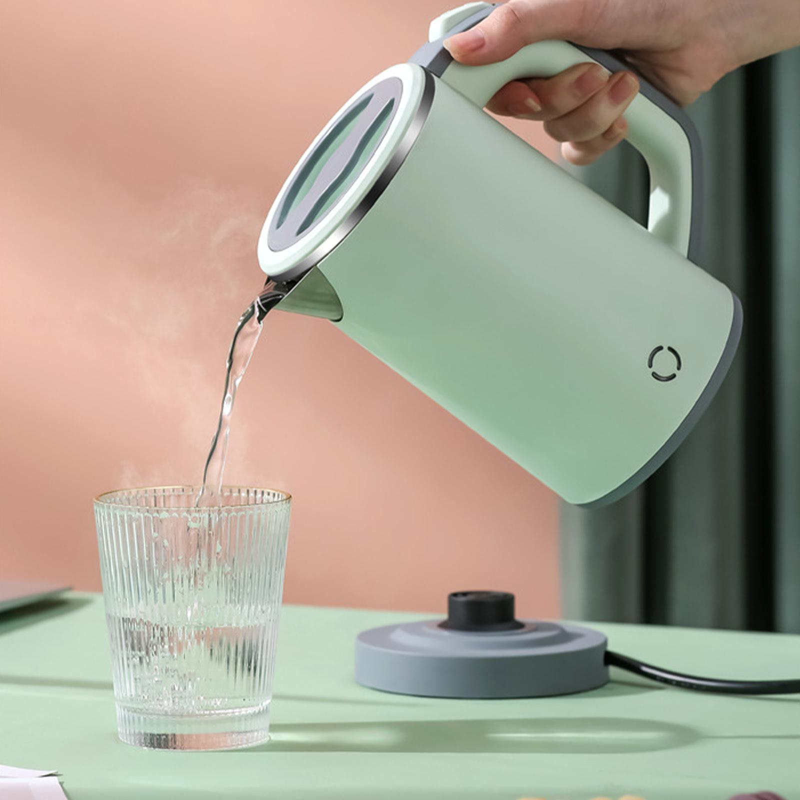 Eine Person gießt Wasser aus einem hellgrünen Wasserkocher in ein Glas auf einem grünen Tisch.