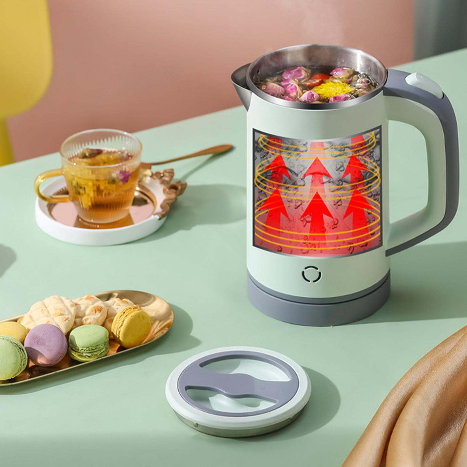 Ein hellgrüner Wasserkocher kocht Wasser mit Kräutern, neben Macarons und einer Teetasse auf einem grünen Tisch.
