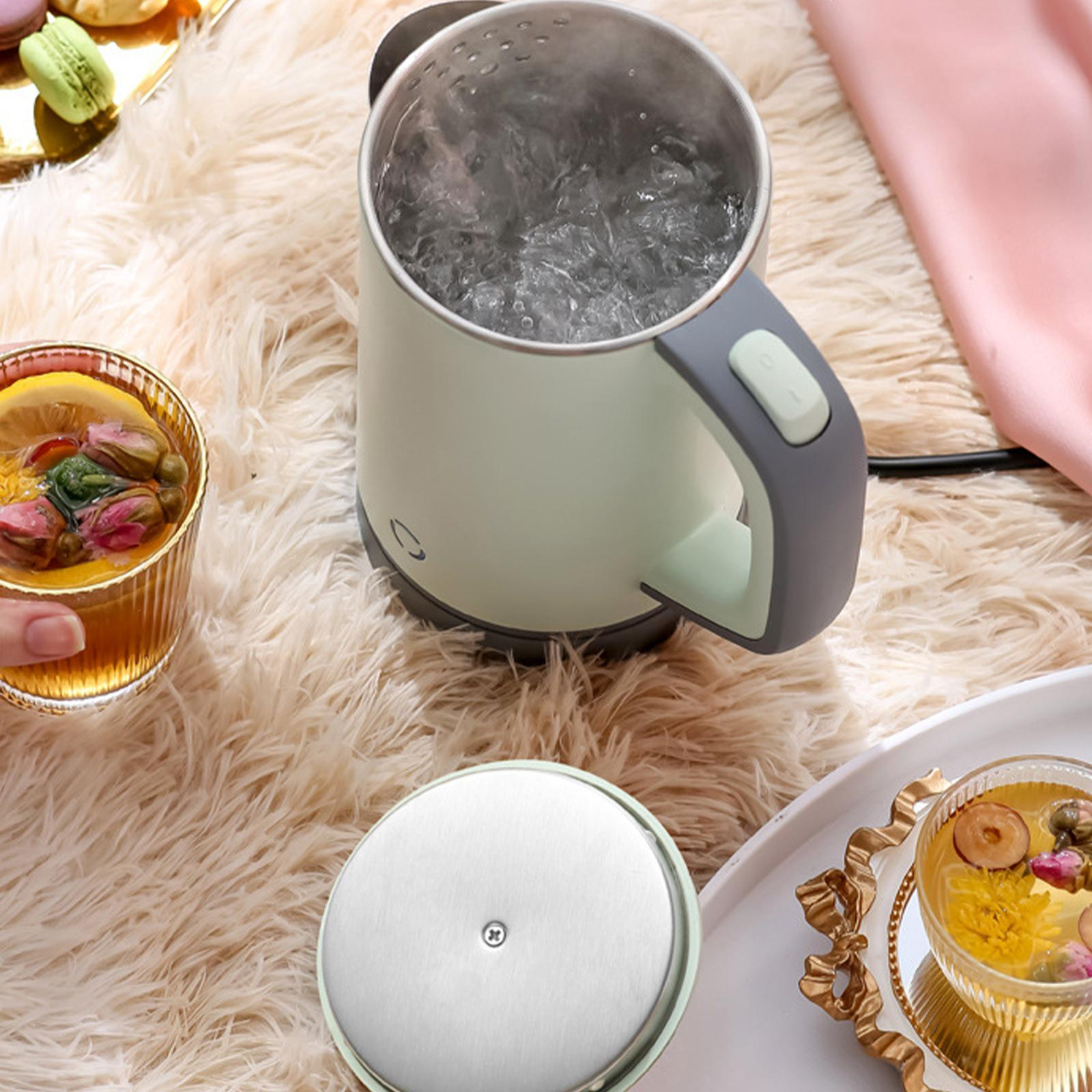 Ein hellgrüner Wasserkocher kocht Wasser in der Nähe von Tee und Macarons auf einer flauschigen weißen Oberfläche.