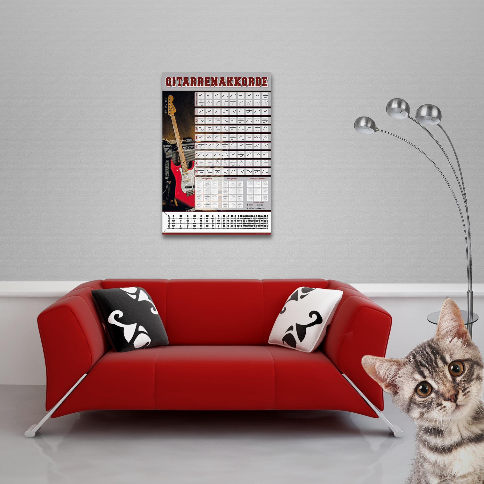 Ein Gitarrenakkord-Poster hängt über einem roten Sofa, während eine Katze in die Kamera schaut.