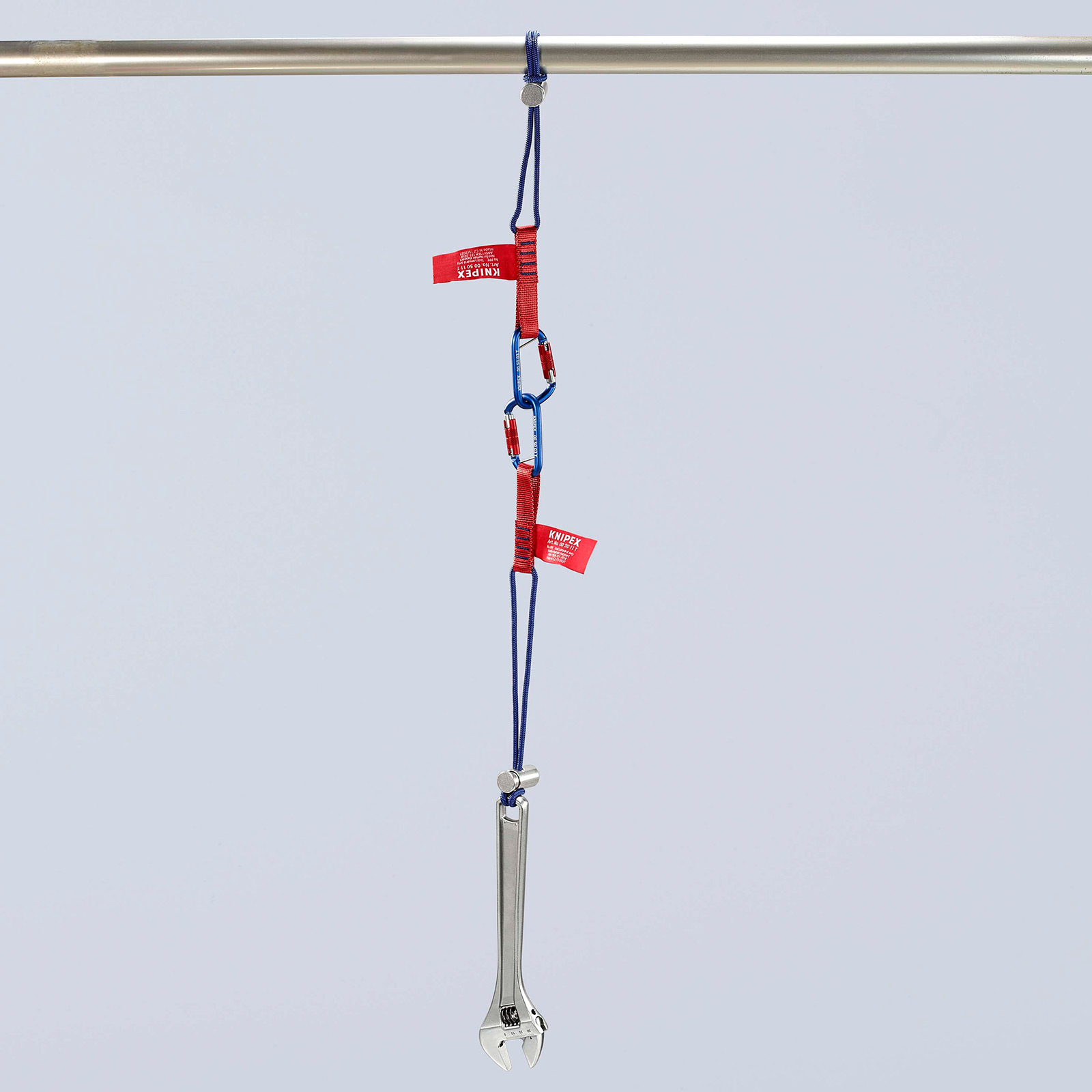Una chiave inglese è appesa a una barra di metallo tramite cinghie blu e rosse con moschettoni.