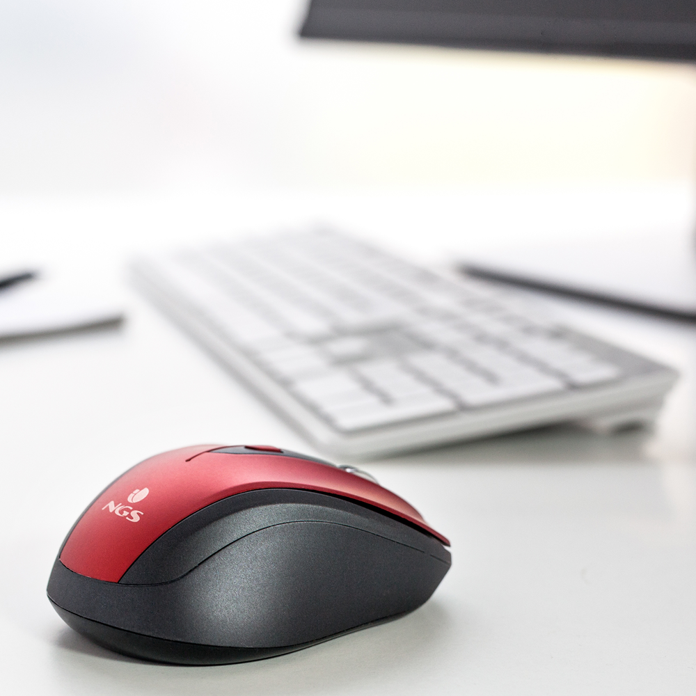 Un mouse wireless NGS rosso e nero si trova su una scrivania bianca con una tastiera sullo sfondo.