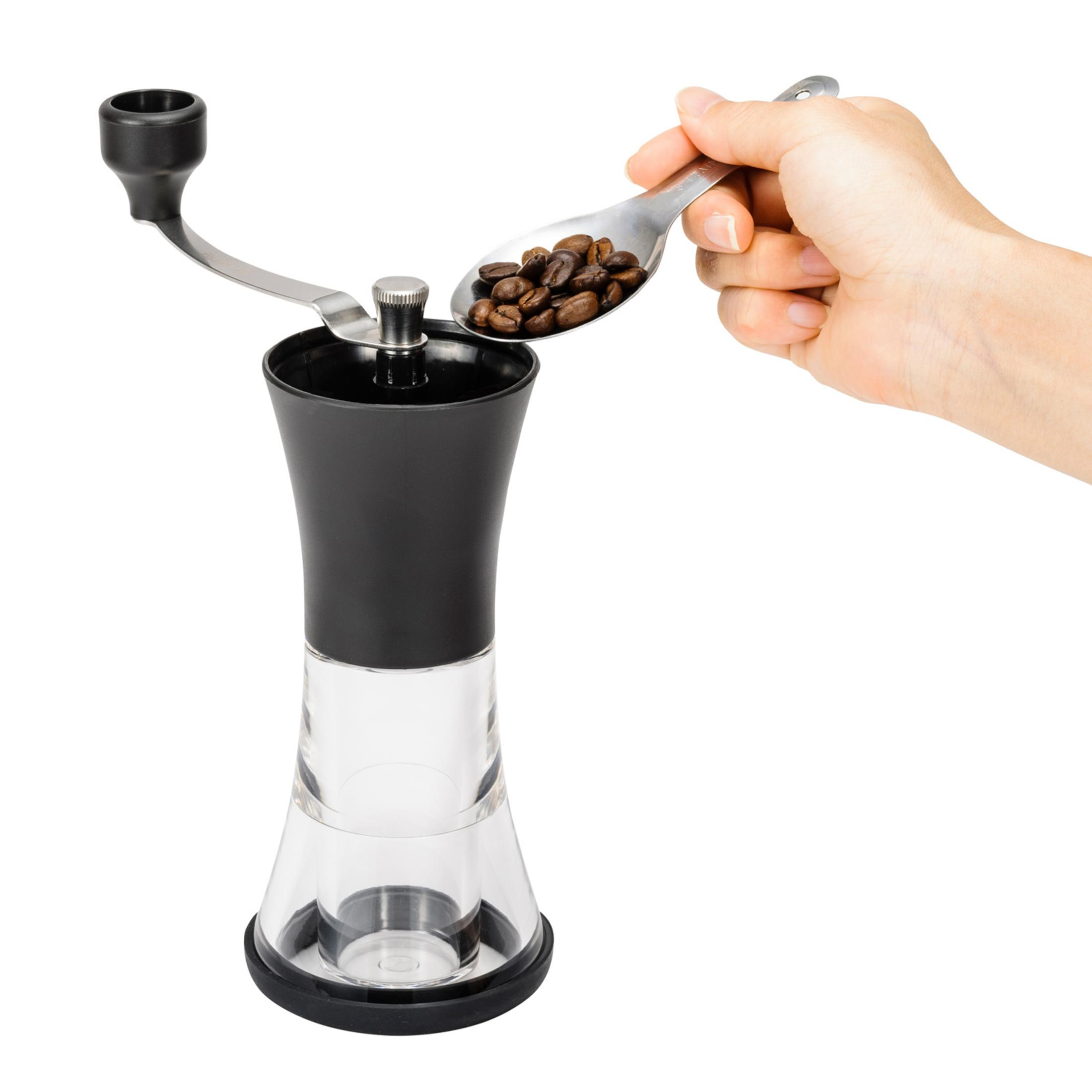 Eine Hand fügt mit einem Löffel Kaffeebohnen zu einer klaren und schwarzen manuellen Mühle hinzu.