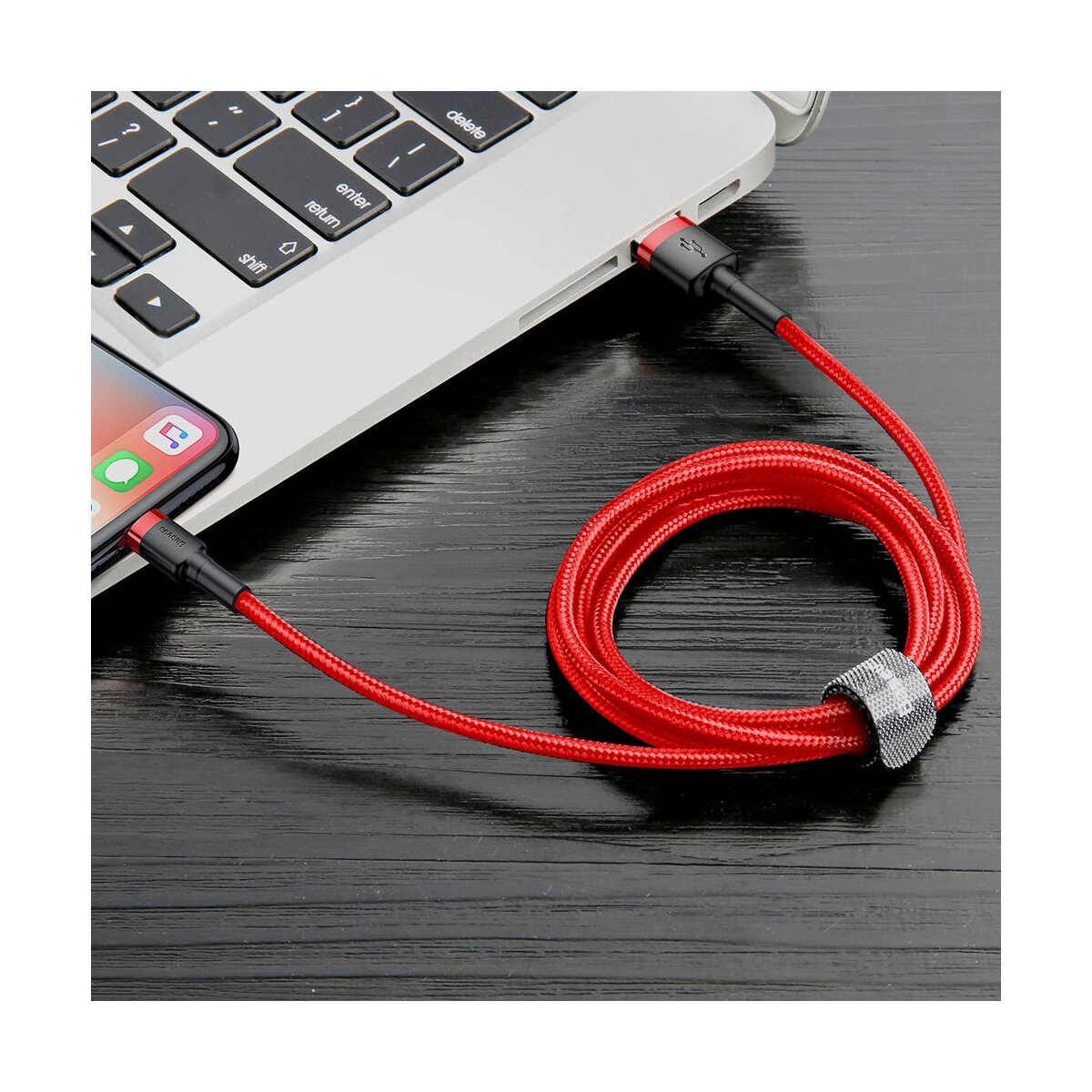 Czerwony kabel Baseus łączy telefon z laptopem na czarnej drewnianej powierzchni.