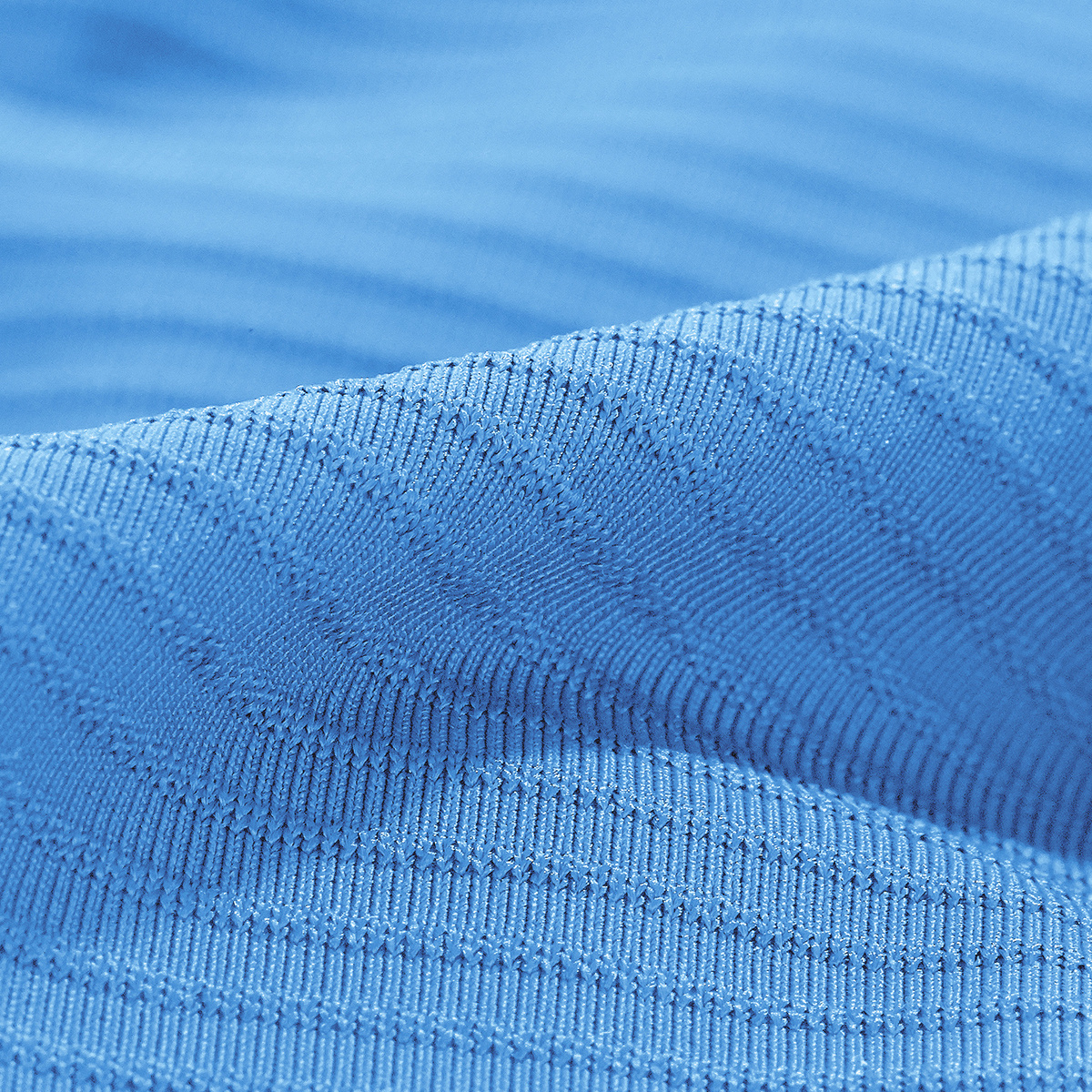 Na zbliżeniu widać niebieską, teksturowaną tkaninę z małymi, powtarzającymi się kwadratowymi wzorami.