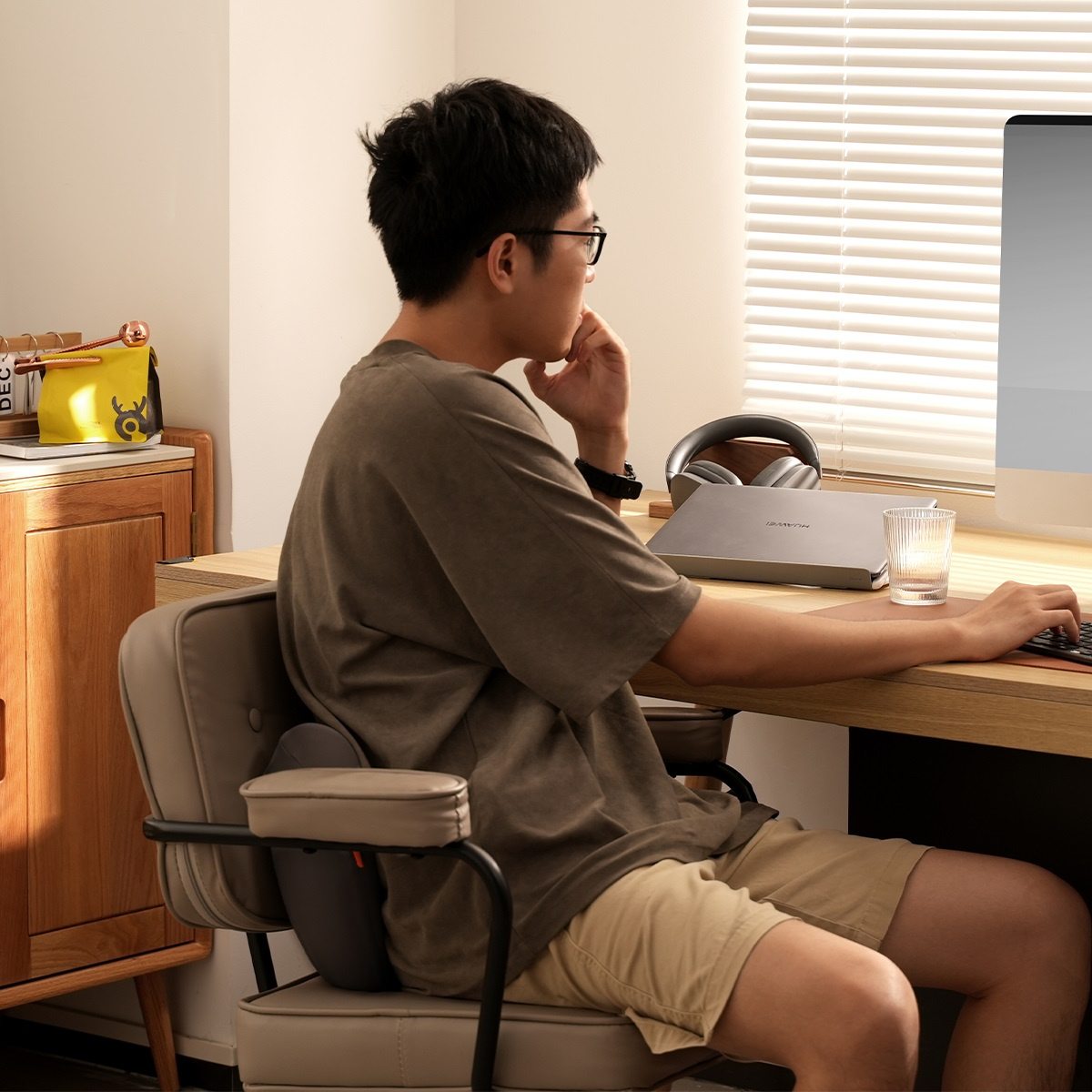 Mężczyzna siedzi na krześle biurowym, używa poduszki podpierającej lędźwie i pracuje przy biurku.