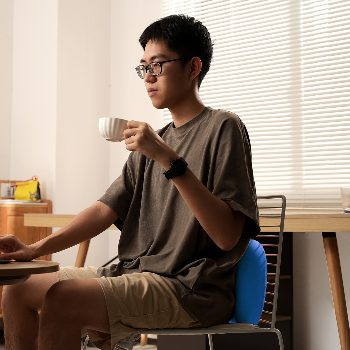 Mężczyzna w okularach siedzi z niebieską poduszką lędźwiową za nim na krześle.