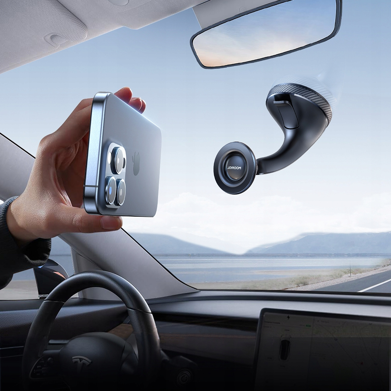 Ręka trzymająca telefon w pobliżu lusterka wstecznego. Telefon jest czarny. Widoczne wnętrze samochodu.