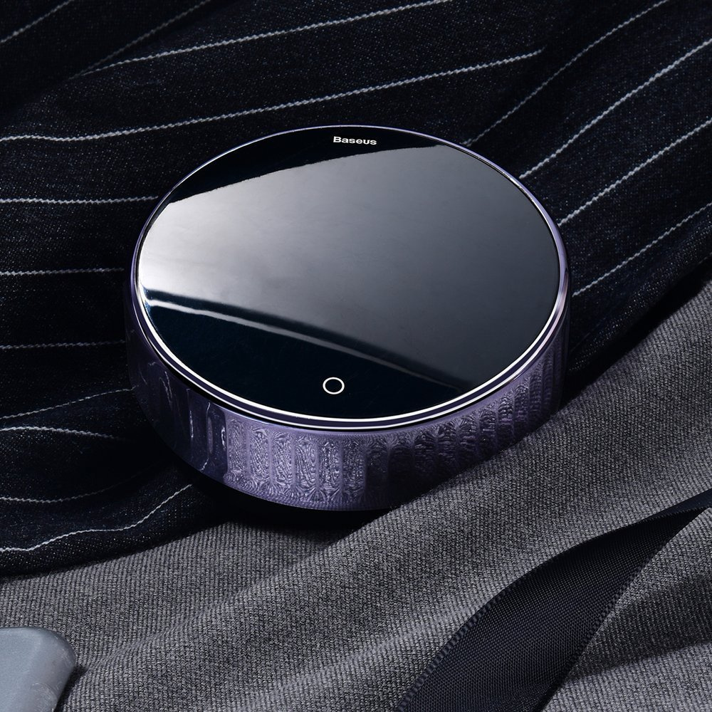 Błyszczące, okrągłe, fioletowe urządzenie Baseus leży na pasiastym szaro-czarnym materiale, odbijając światło.