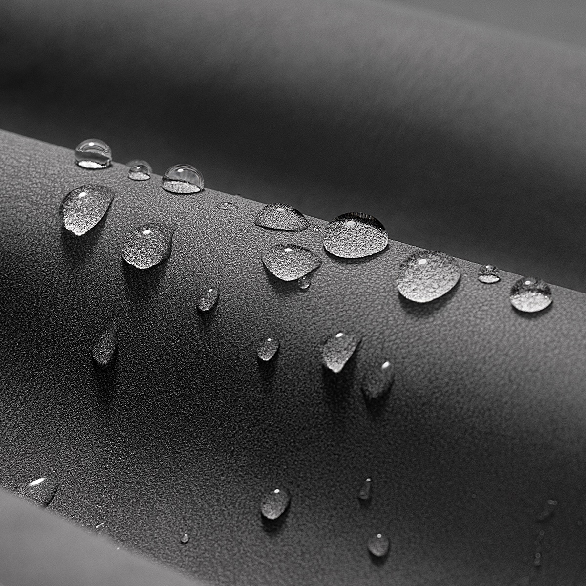 Zbliżenie kropli wody na szarej powierzchni, tworzące teksturowany i odblaskowy wzór.