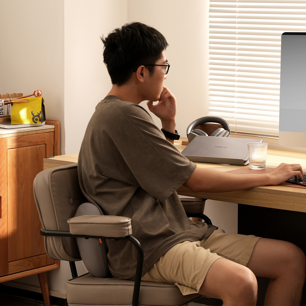 Mężczyzna siedzi przy biurku z szarą poduszką lędźwiową na krześle.