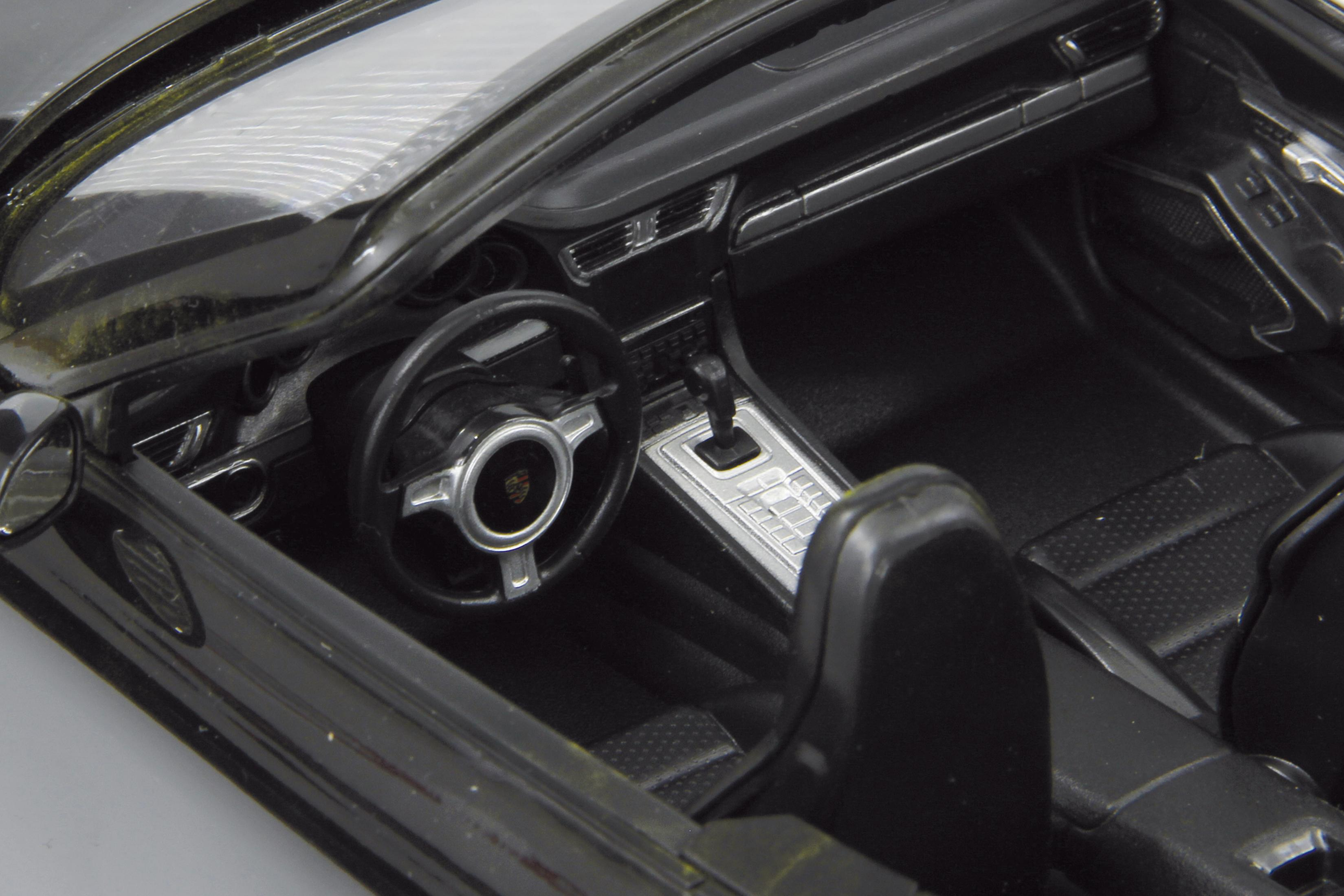 Nahaufnahme eines schwarzen Autoinnenraums mit einem Lenkrad mit Porsche-Logo.
