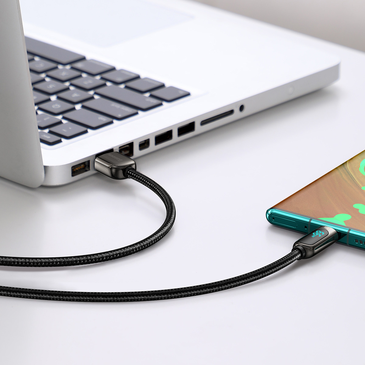 Laptop i telefon połączone kablem USB-C z cyfrowym wyświetlaczem pokazującym 99 W do ładowania.