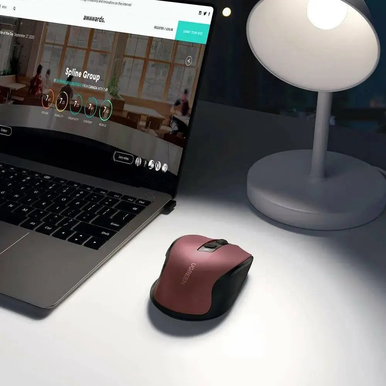 Obraz przedstawia różowo-czerwoną mysz UGREEN, laptopa i lampę, wszystko na białym biurku.