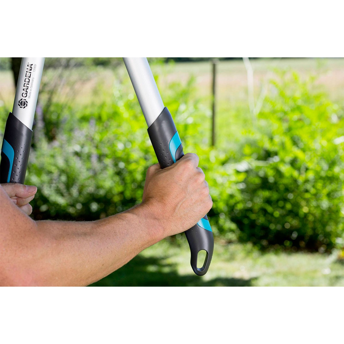 Una mano afferra cesoie grigie e nere con accenti color teal in un cortile erboso.
