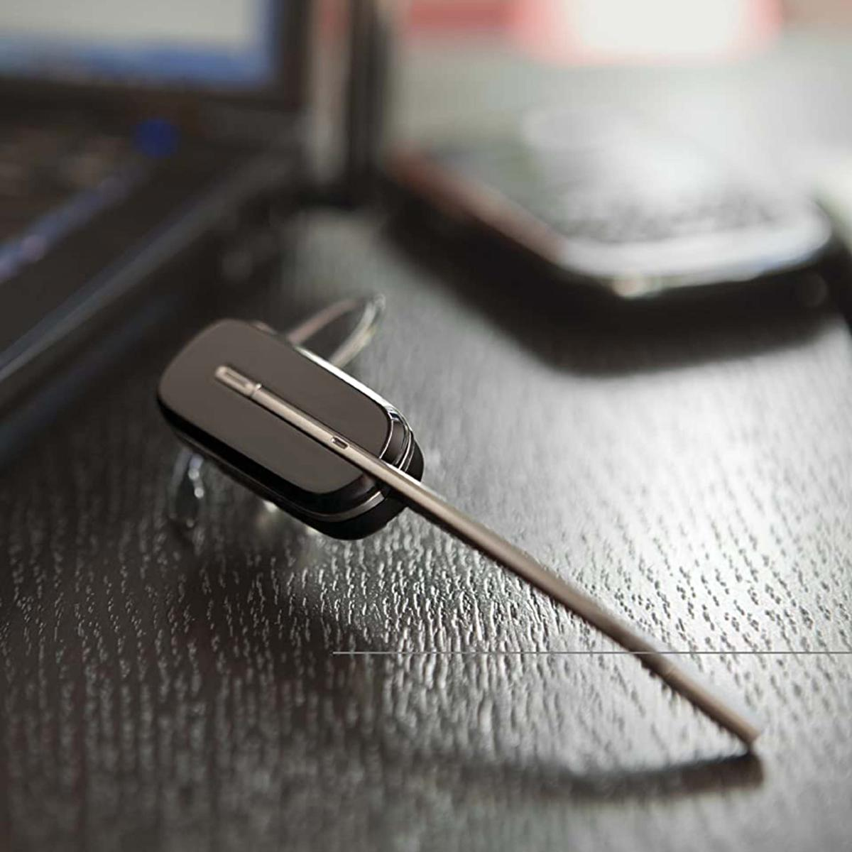 Un auricolare wireless nero con microfono su una superficie di legno scuro. Parte di un laptop è visibile.