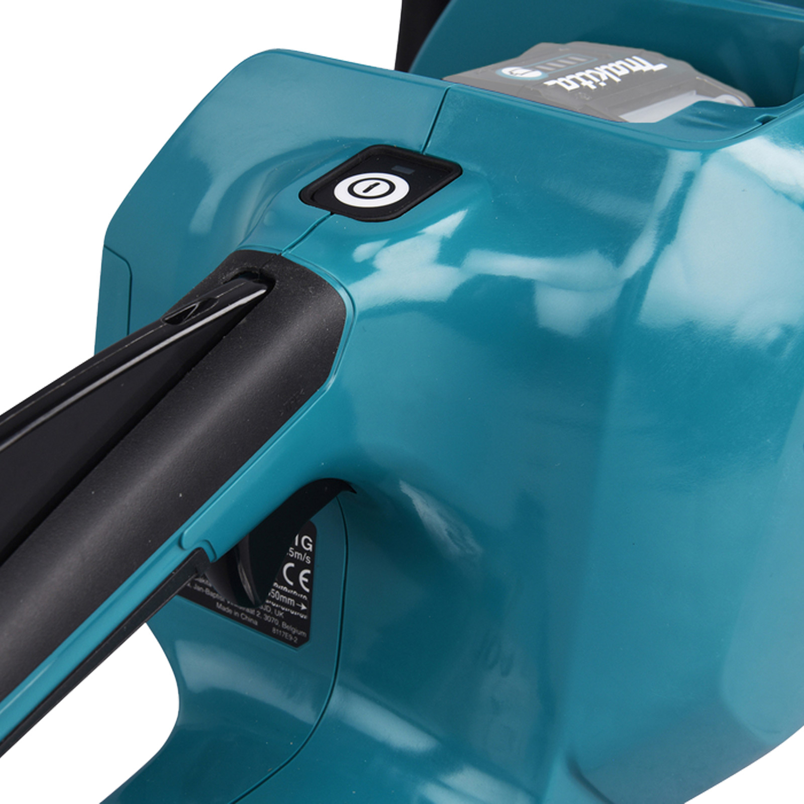 Nahaufnahme des türkisfarbenen Makita Kettensägerumpfs mit Batteriefach und Einschaltknopf auf weißem Hintergrund.