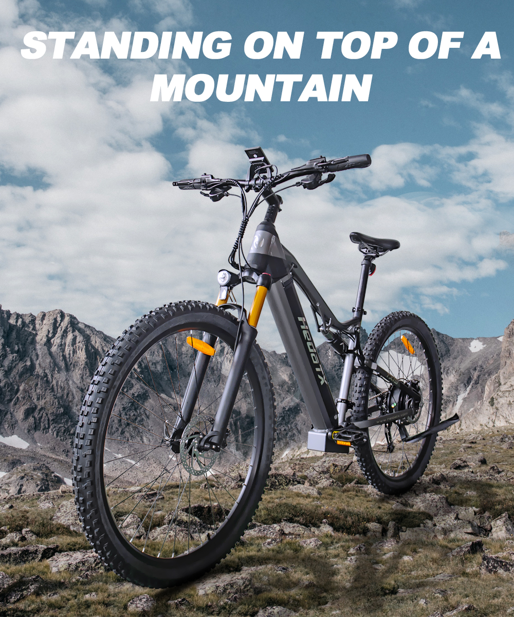Szary elektryczny rower górski na szczycie góry z pochmurnym błękitnym niebem w tle.