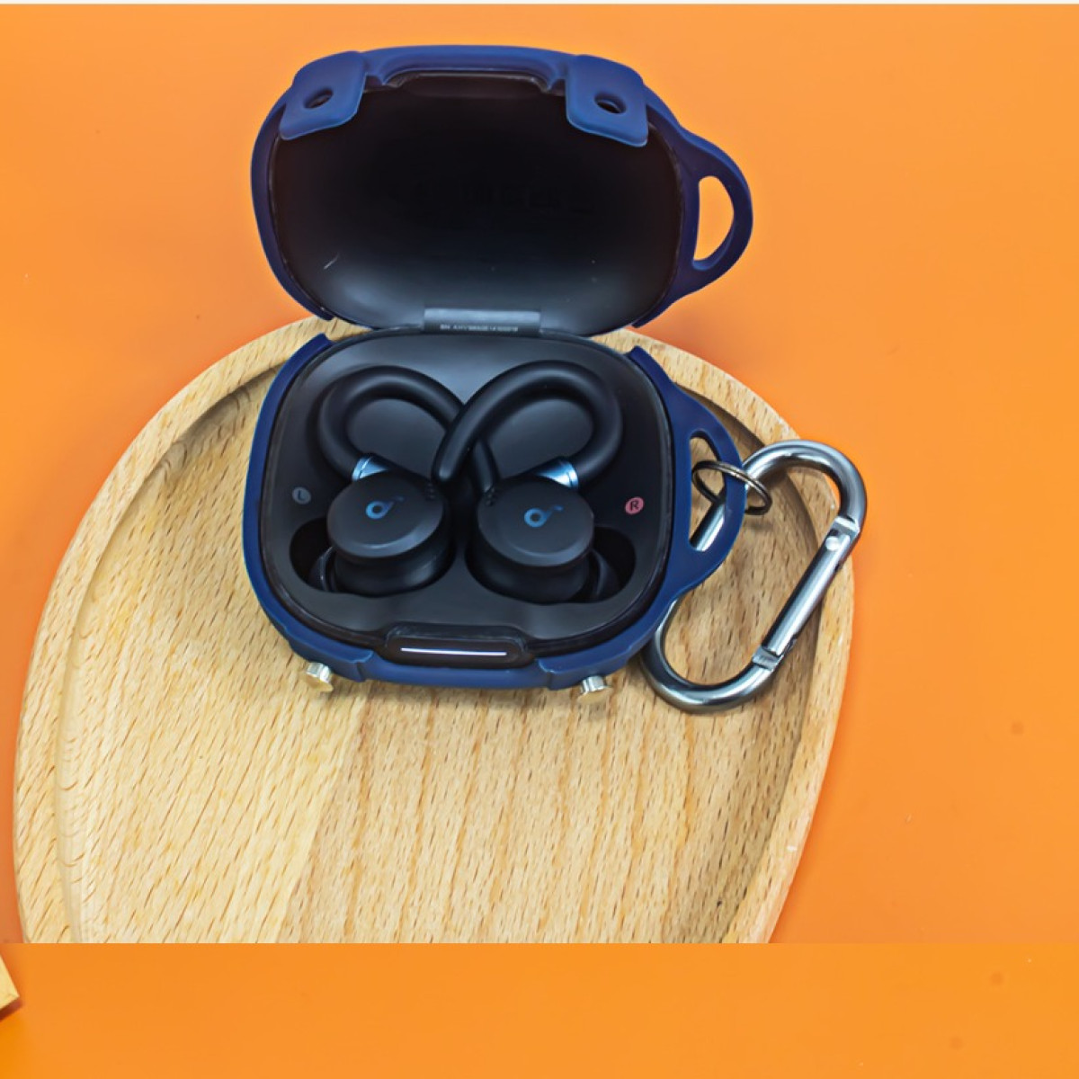 Ein blaues Ohrhörer-Etui mit schwarzen Ohrhörern darin, auf einem Holztablett vor orangefarbenem Hintergrund platziert.