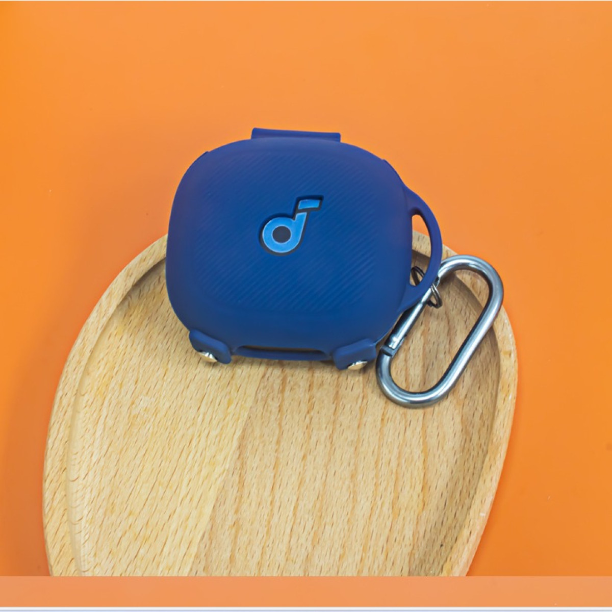 Ein blaues Ohrhörer-Etui auf einem Holztablett vor orangefarbenem Hintergrund. Das Etui ist geschlossen.